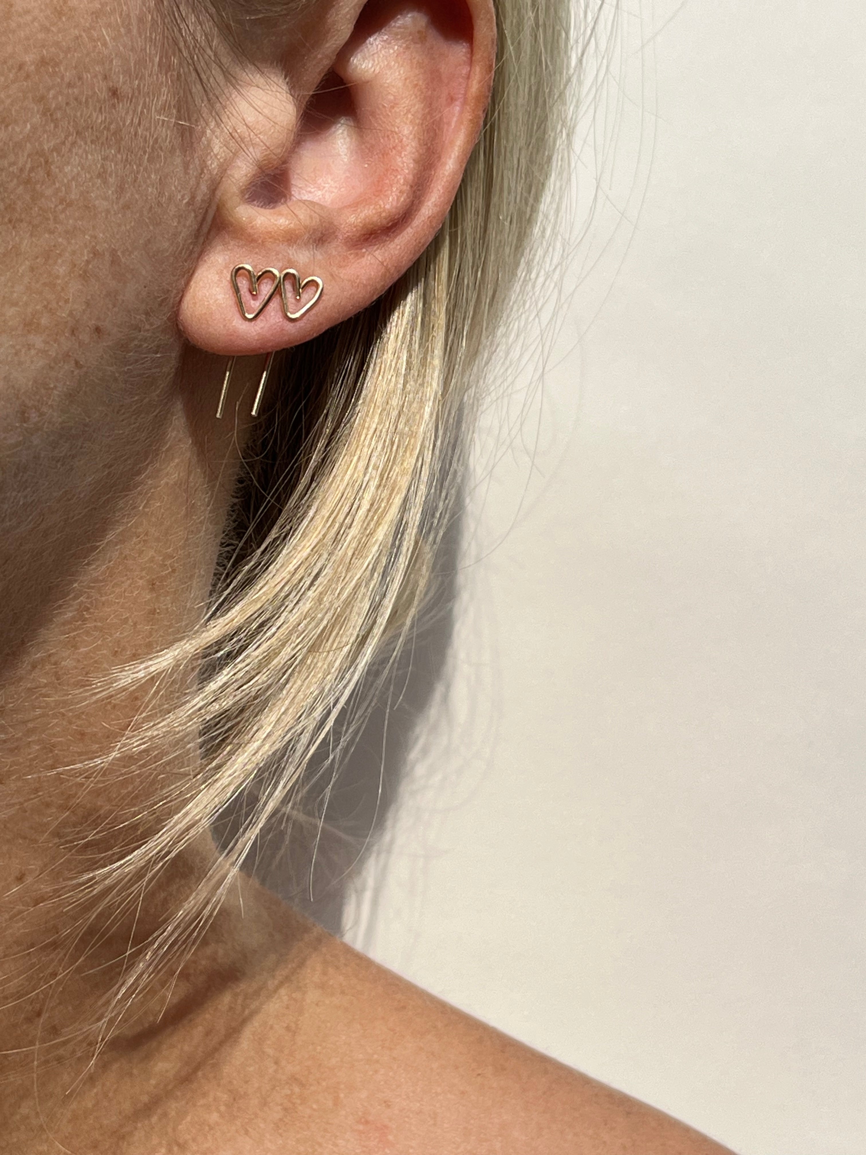 close up of woman's ear with two wire heart earrings in two ear piercings 