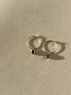 Product shot of Thalken 14k gold 12mm hoop earrings paired with small pear-shaped black spinel drop charms