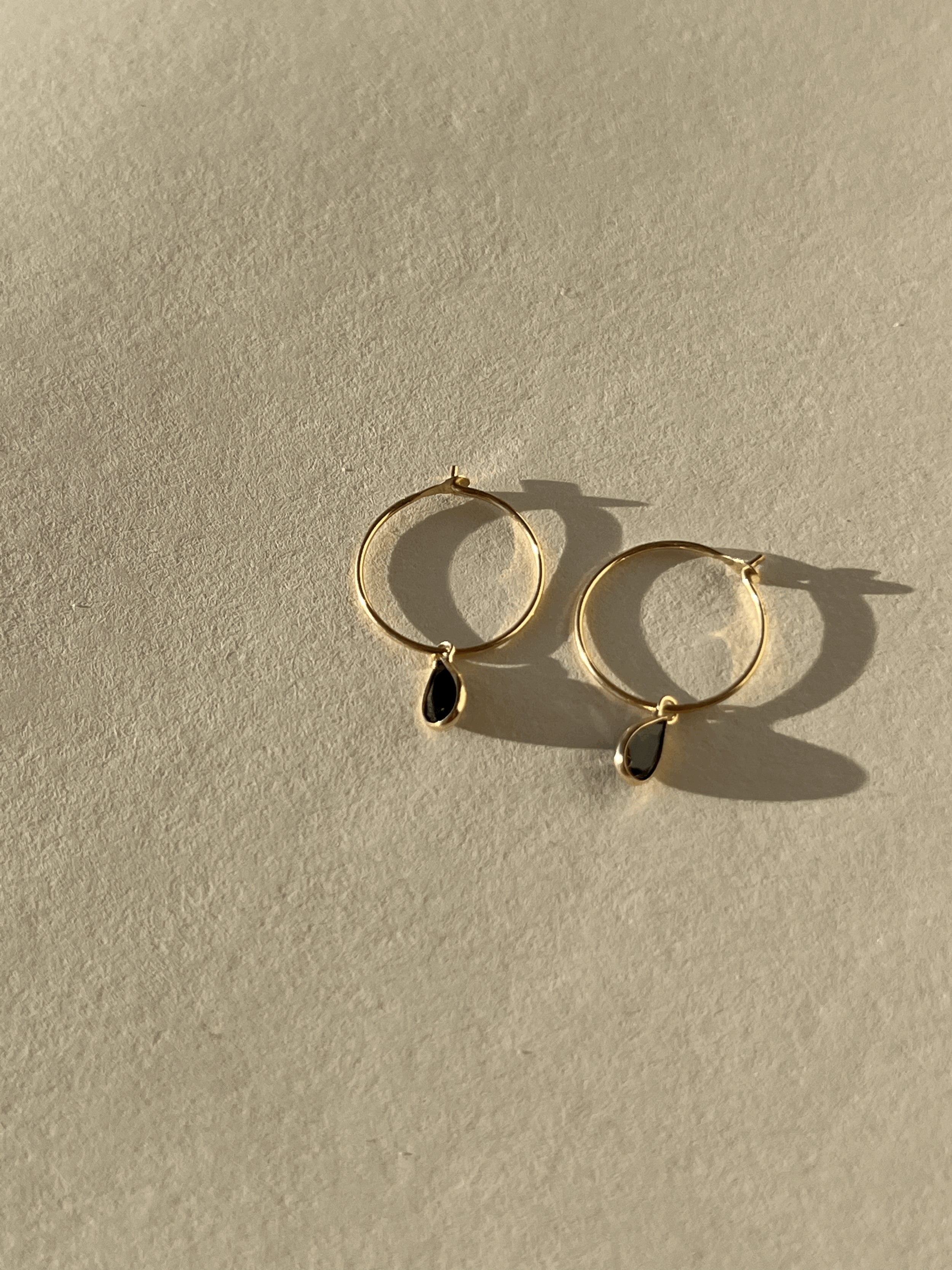 Product shot of Thalken 14k gold 12mm hoop earrings paired with small pear-shaped black spinel drop charms