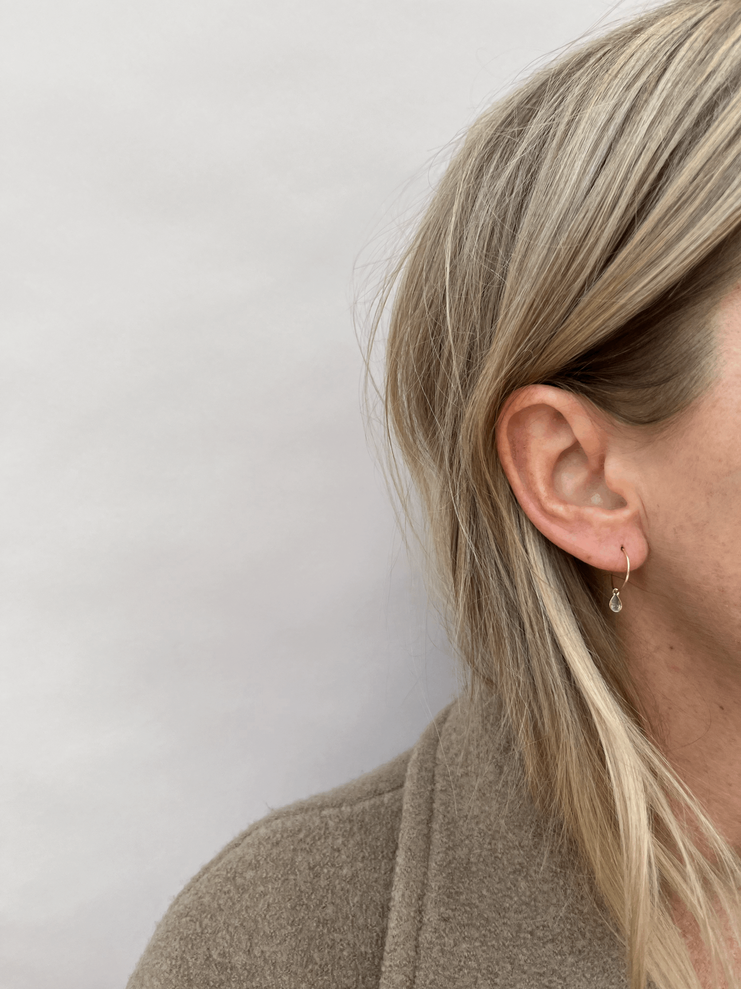 Model wearing Thalken 14k gold 10mm hoop earring with a small pear-shaped drop for a dainty, elegant everyday look