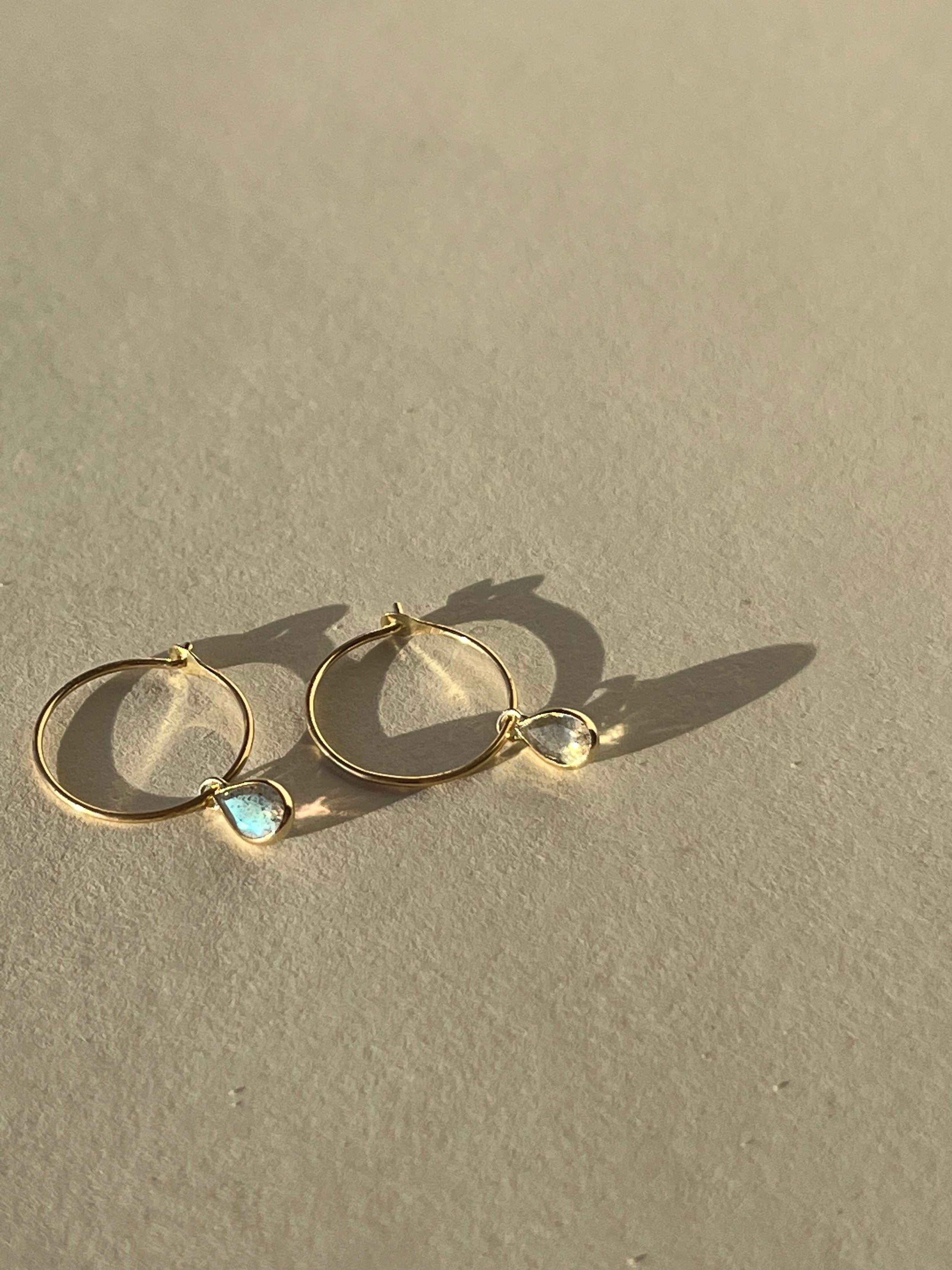 Close-up of Thalken 14k gold 10mm hoop earrings paired with small pear-shaped drop charms, showcasing minimalist and timeless design