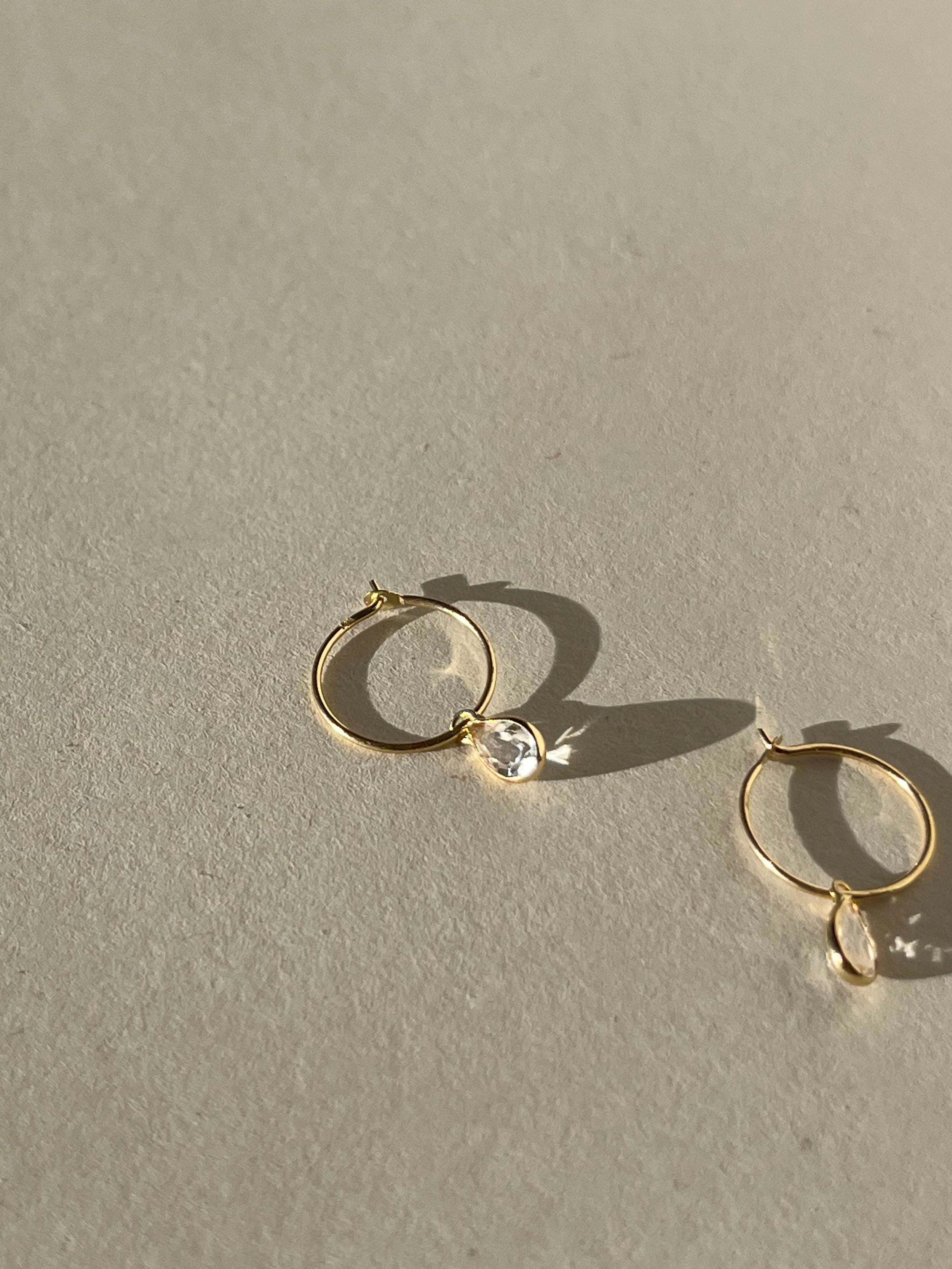 Close-up of Thalken 14k gold 10mm hoop earrings with small pear-shaped white topaz drop charms, highlighting minimalist fine jewelry design