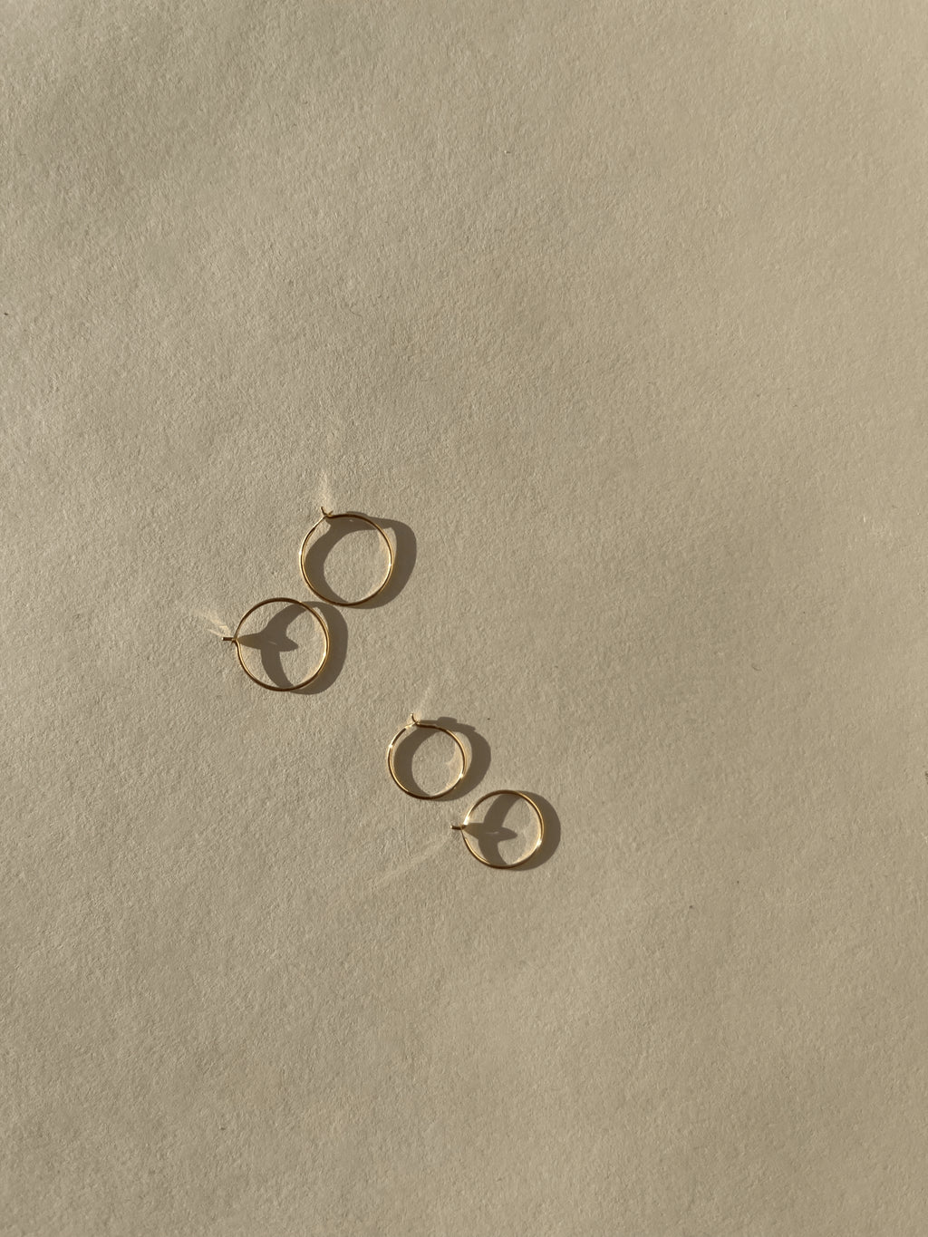 Two pairs of Thalken’s 14k solid gold dainty hoop earrings on a neutral background, showing both 10mm and 12mm sizes