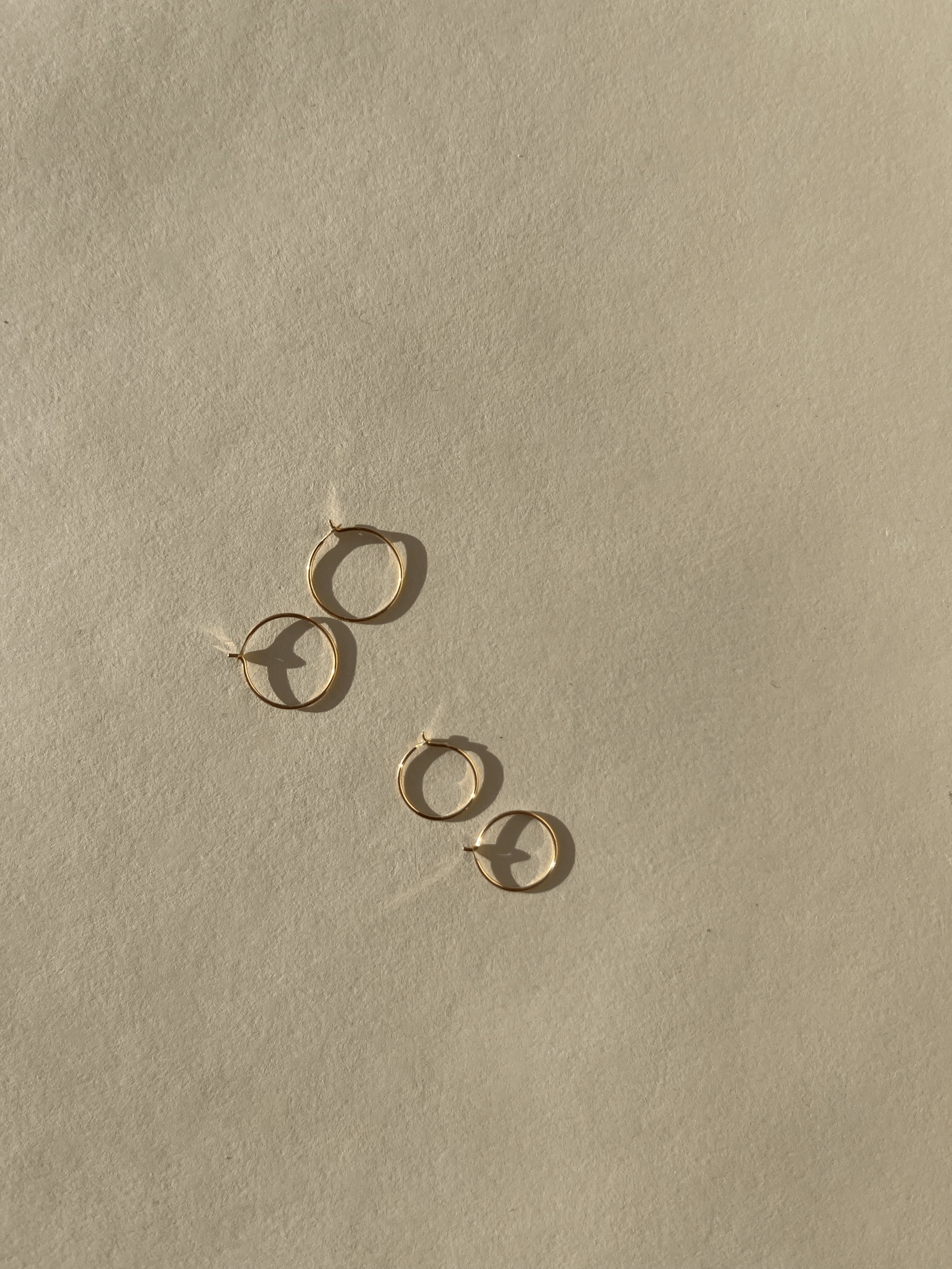 Two pairs of Thalken’s 14k solid gold dainty hoop earrings on a neutral background, showing both 10mm and 12mm sizes
