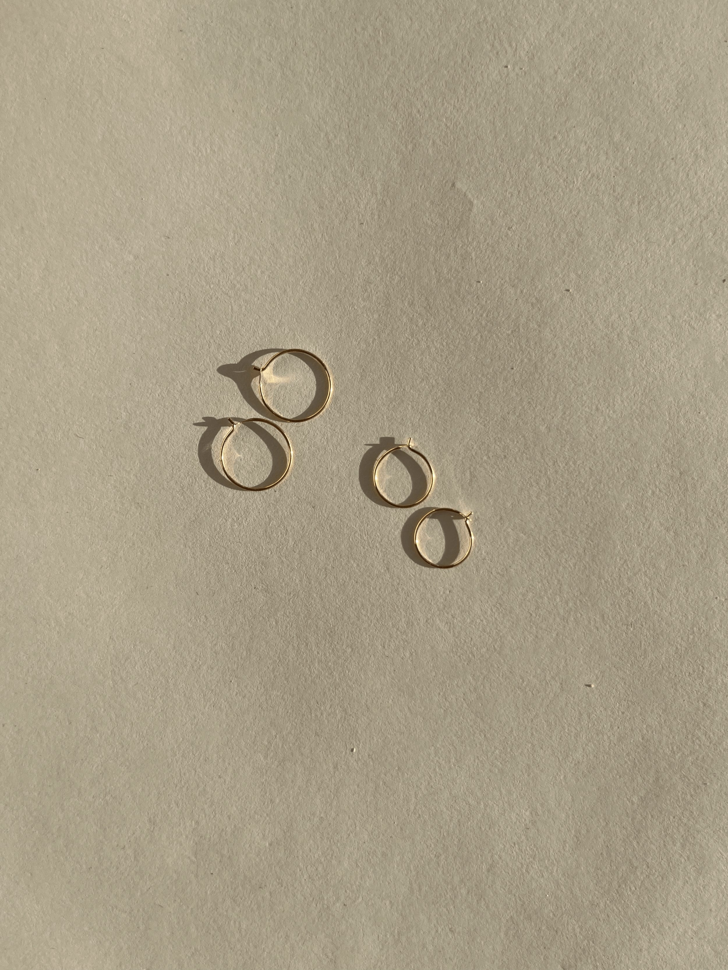 Flat-lay of Thalken’s 14k solid gold dainty hoop earrings in 10mm and 12mm sizes, displayed together on a neutral background