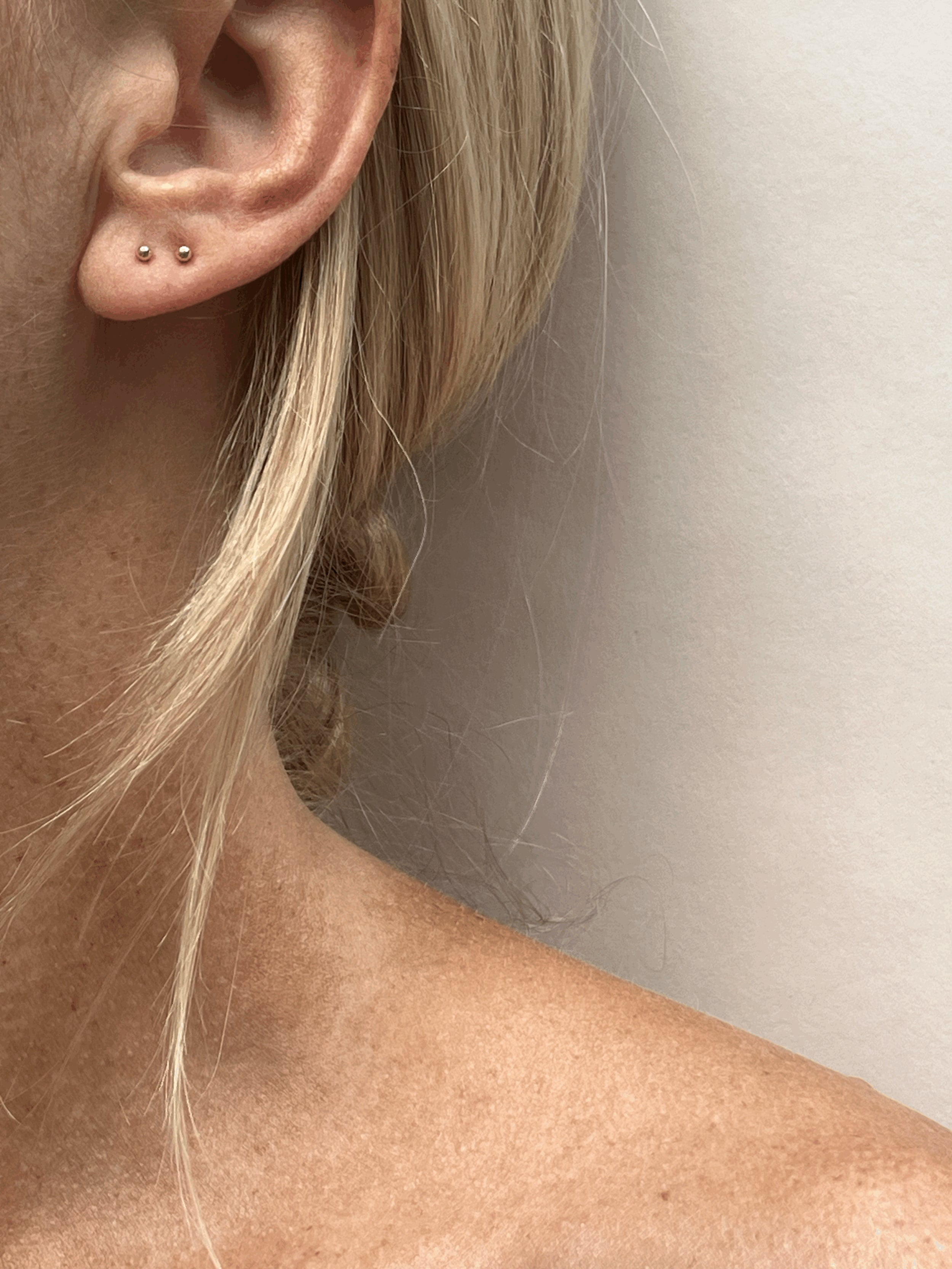 Model wearing 14k solid gold 2mm ball stud earrings in her first and second ear piercings, showcasing minimalist styling