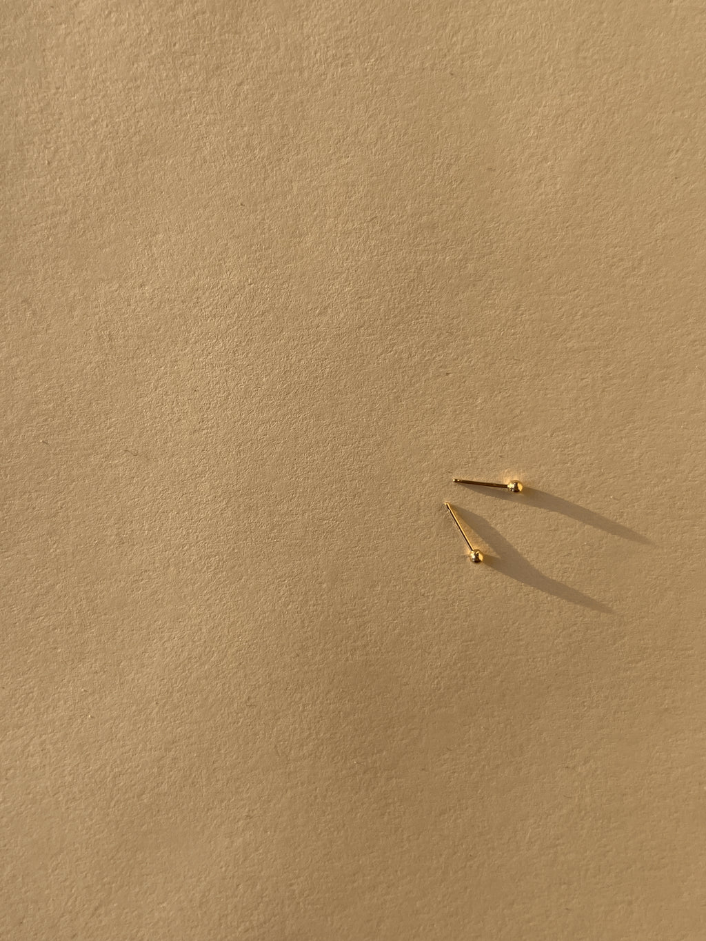 Pair of 2mm 14k solid gold ball stud earrings displayed on a neutral background
