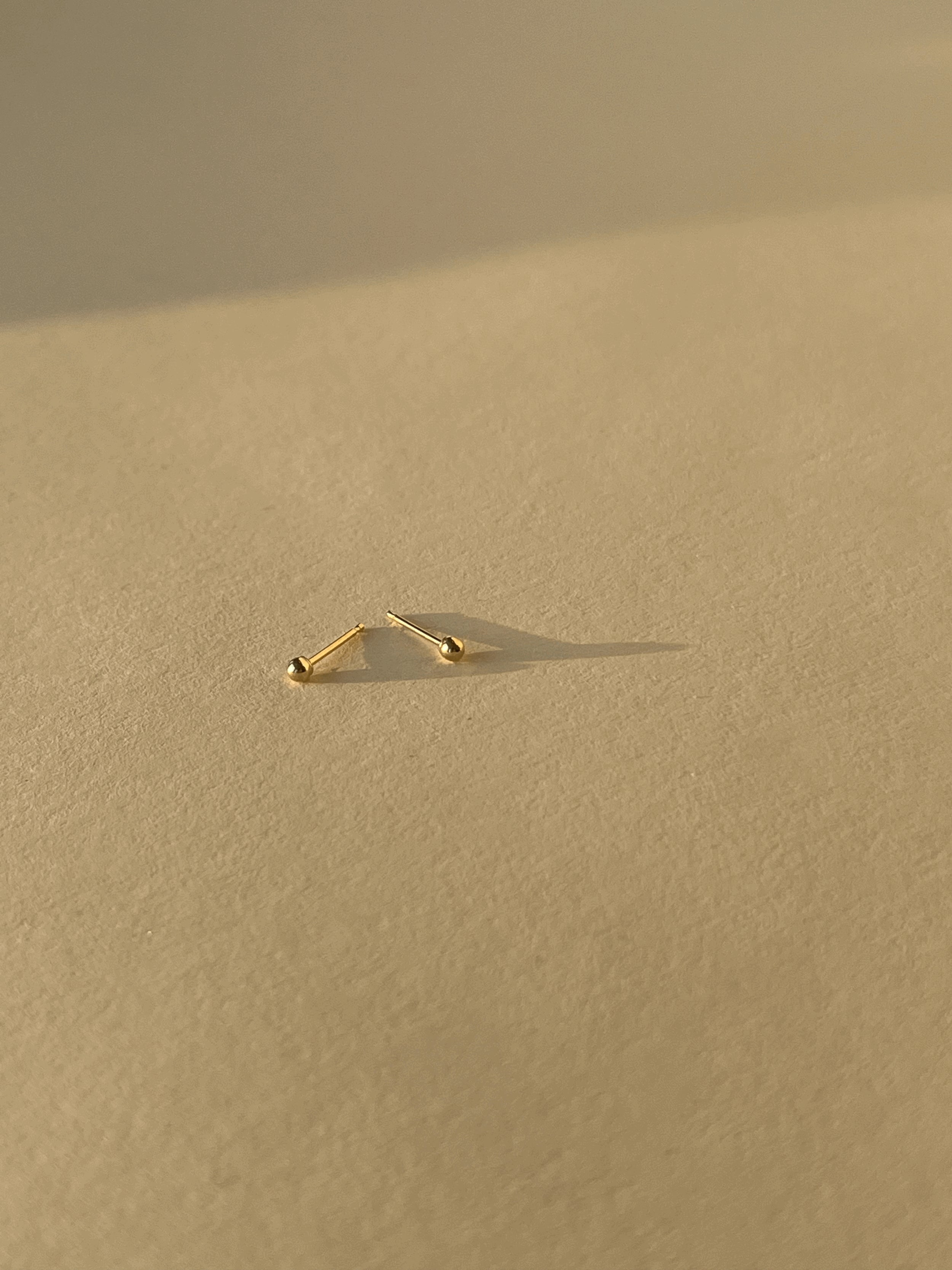 Close-up of 2mm 14k solid gold ball stud earring pair on a neutral background, highlighting their petite size and polished finish