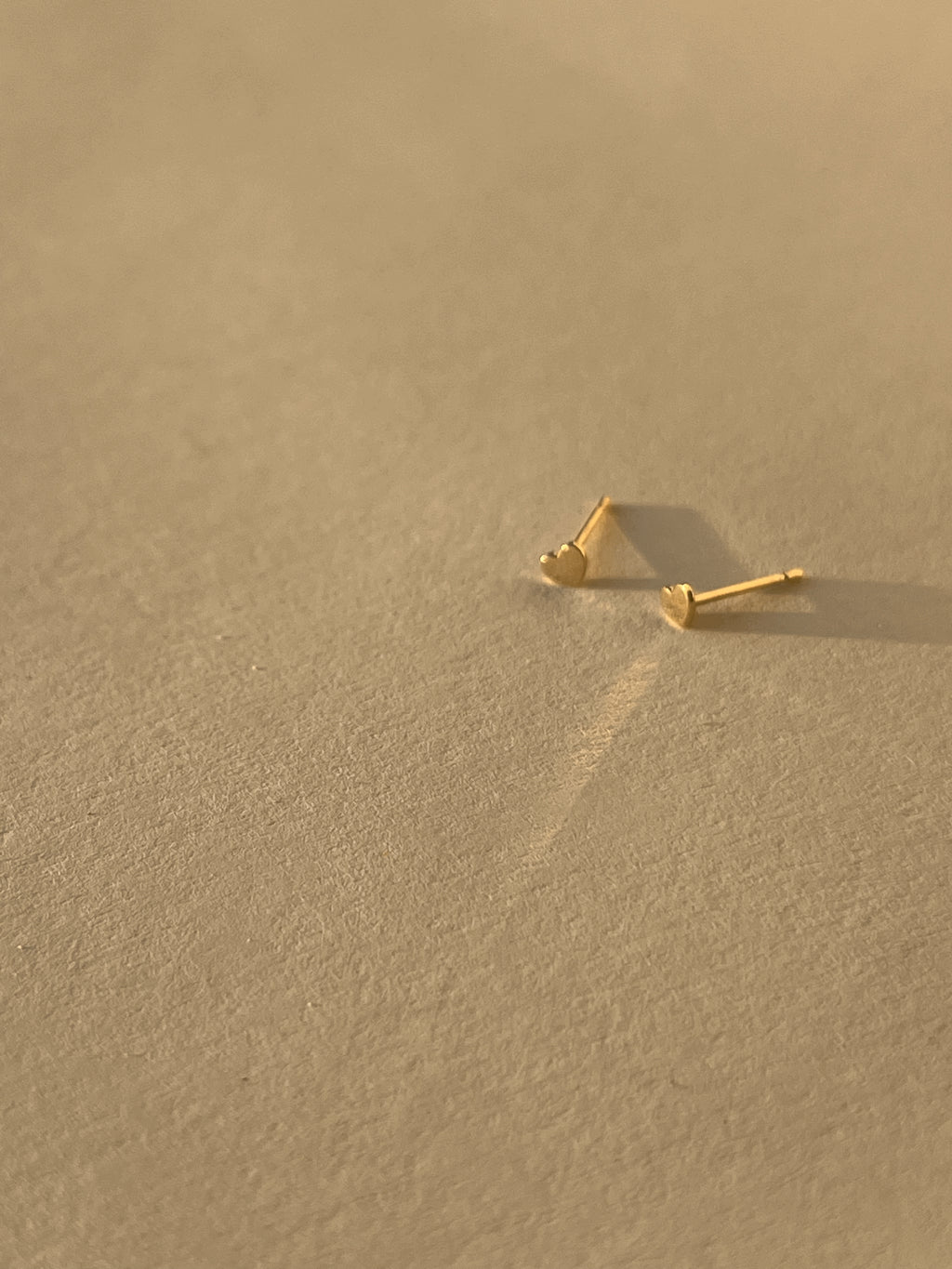 Pair of 14k solid yellow gold 3mm heart stud earrings displayed on a neutral background from different angles