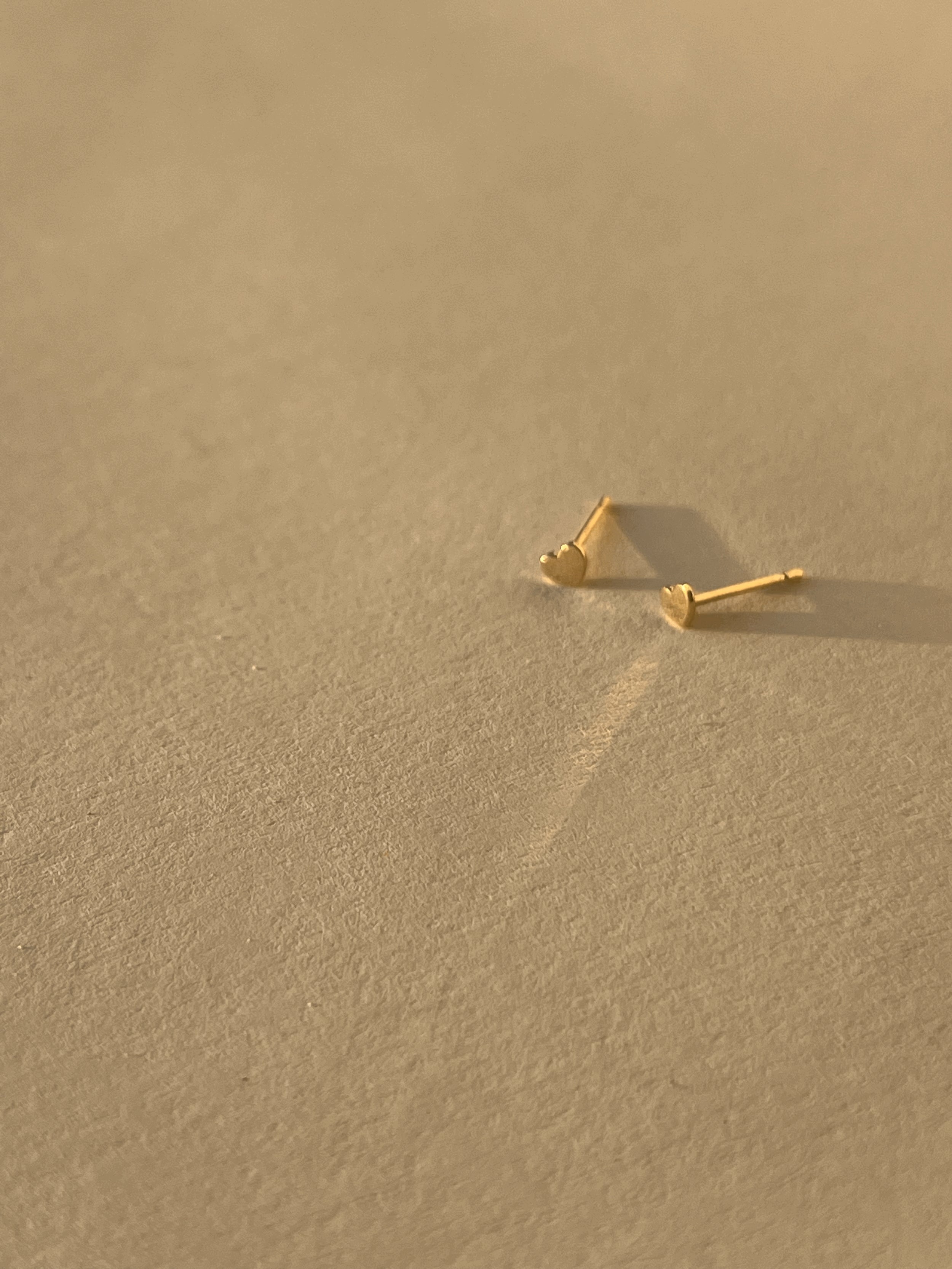 Pair of 14k solid yellow gold 3mm heart stud earrings displayed on a neutral background from different angles