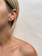 Model wearing Thalken’s Tiny Skull Stud Earrings in her first and second ear piercings; 14k solid yellow gold with black enamel eyes, styled with layered earrings