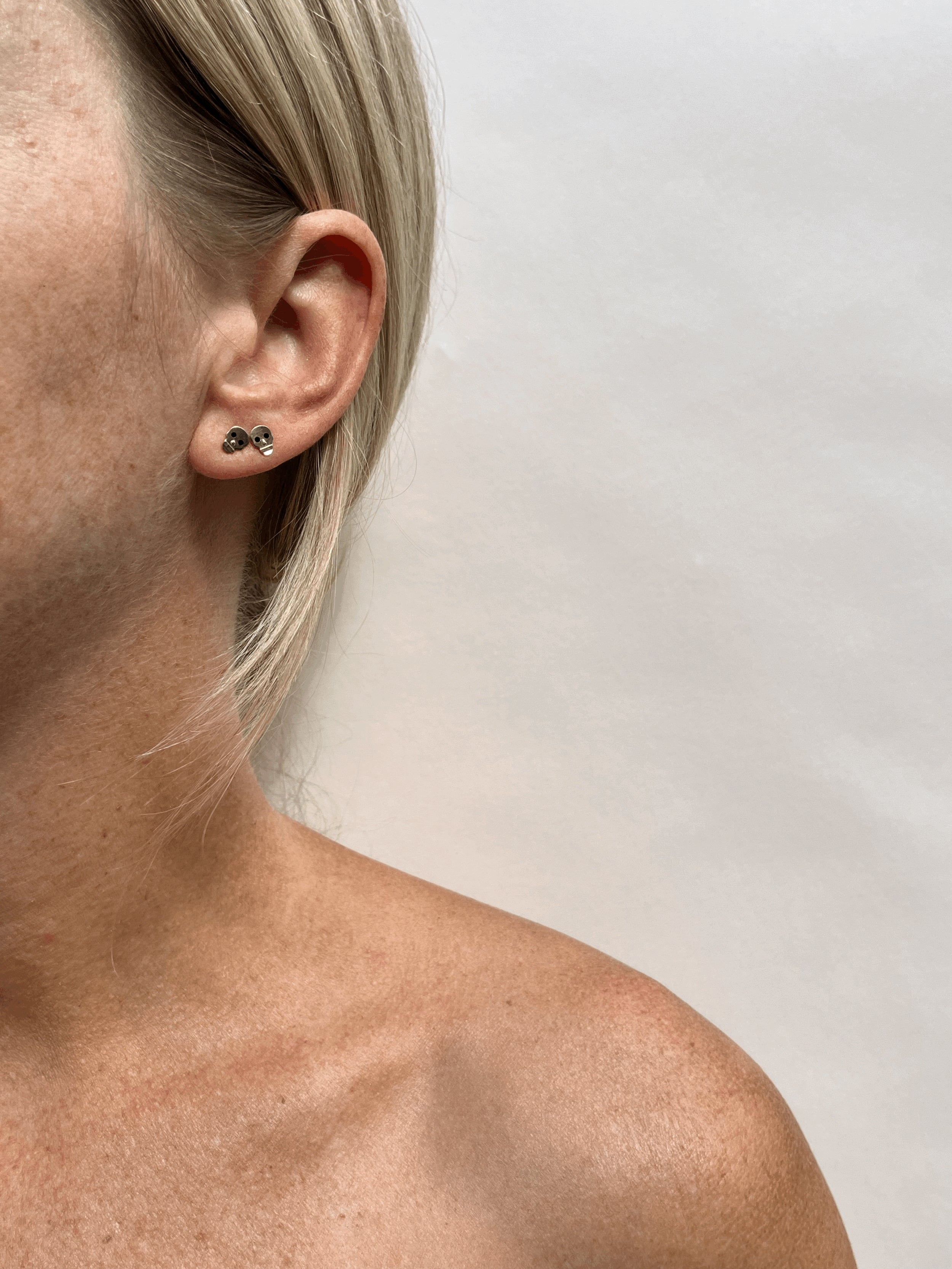 Model wearing Thalken’s Tiny Skull Stud Earrings in her first and second ear piercings; 14k solid yellow gold with black enamel eyes, styled with layered earrings