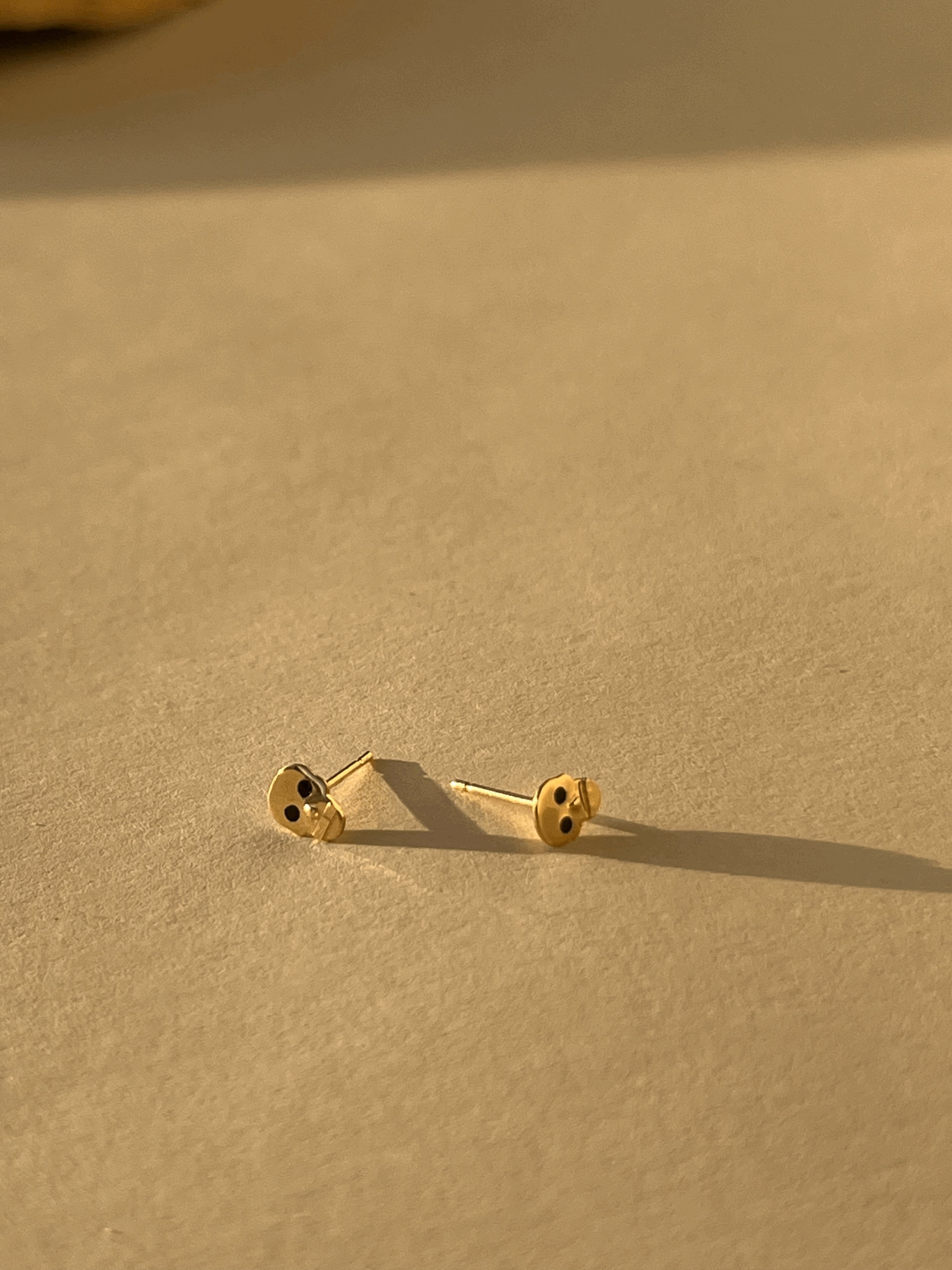 Pair of Tiny Skull Stud Earrings displayed flat on a neutral background, showcasing gold skull shape and black enamel eye detailing