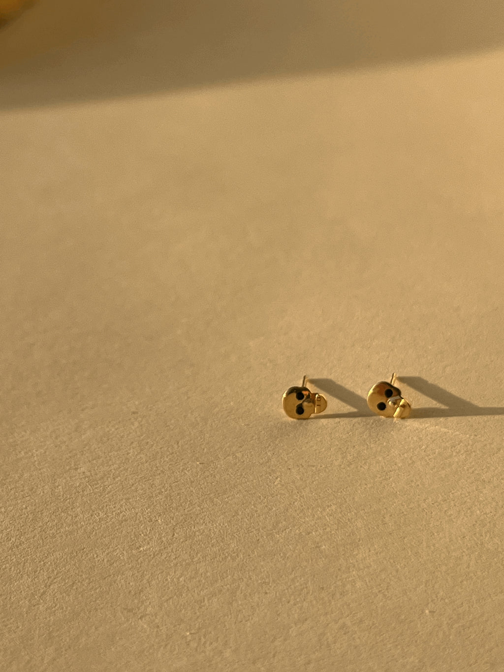 Pair of Tiny Skull Stud Earrings front faced, showcasing gold skull shape and black enamel eye detailing