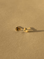Close-up of a pair of Tiny Skull Stud Earrings displayed on a neutral background, showcasing gold skull shape and black enamel eye detailing