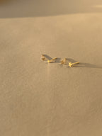 Wide shot of the 3mm and 4mm Tiny Star Stud Earrings in 14k solid yellow gold placed together on a soft, neutral surface