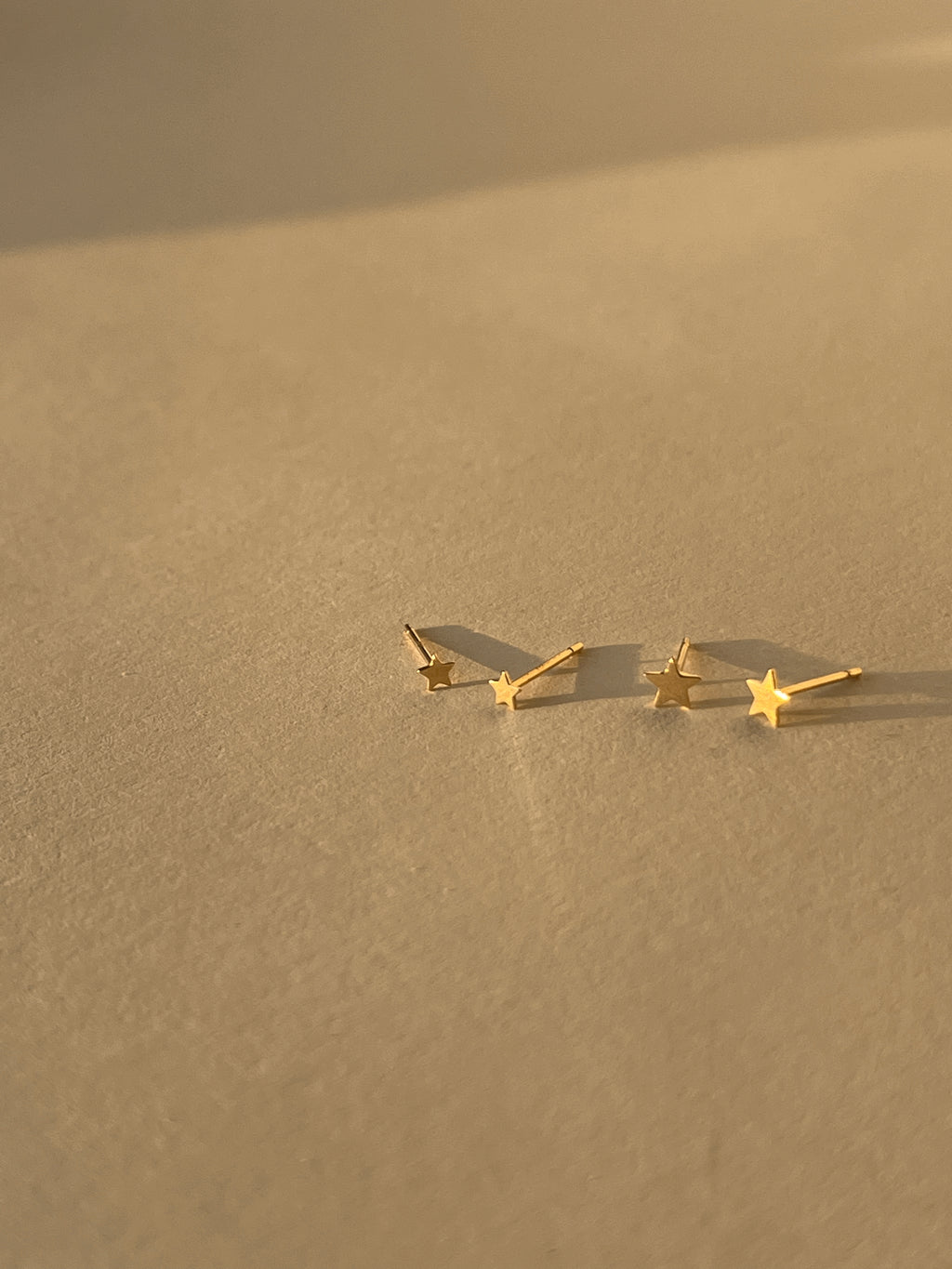 Close-up of the 3mm and 4mm Tiny Star Stud Earrings in 14k solid yellow gold displayed side by side on a neutral backdrop