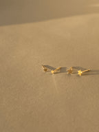 Close-up of the 3mm and 4mm Tiny Star Stud Earrings in 14k solid yellow gold displayed side by side on a neutral backdrop