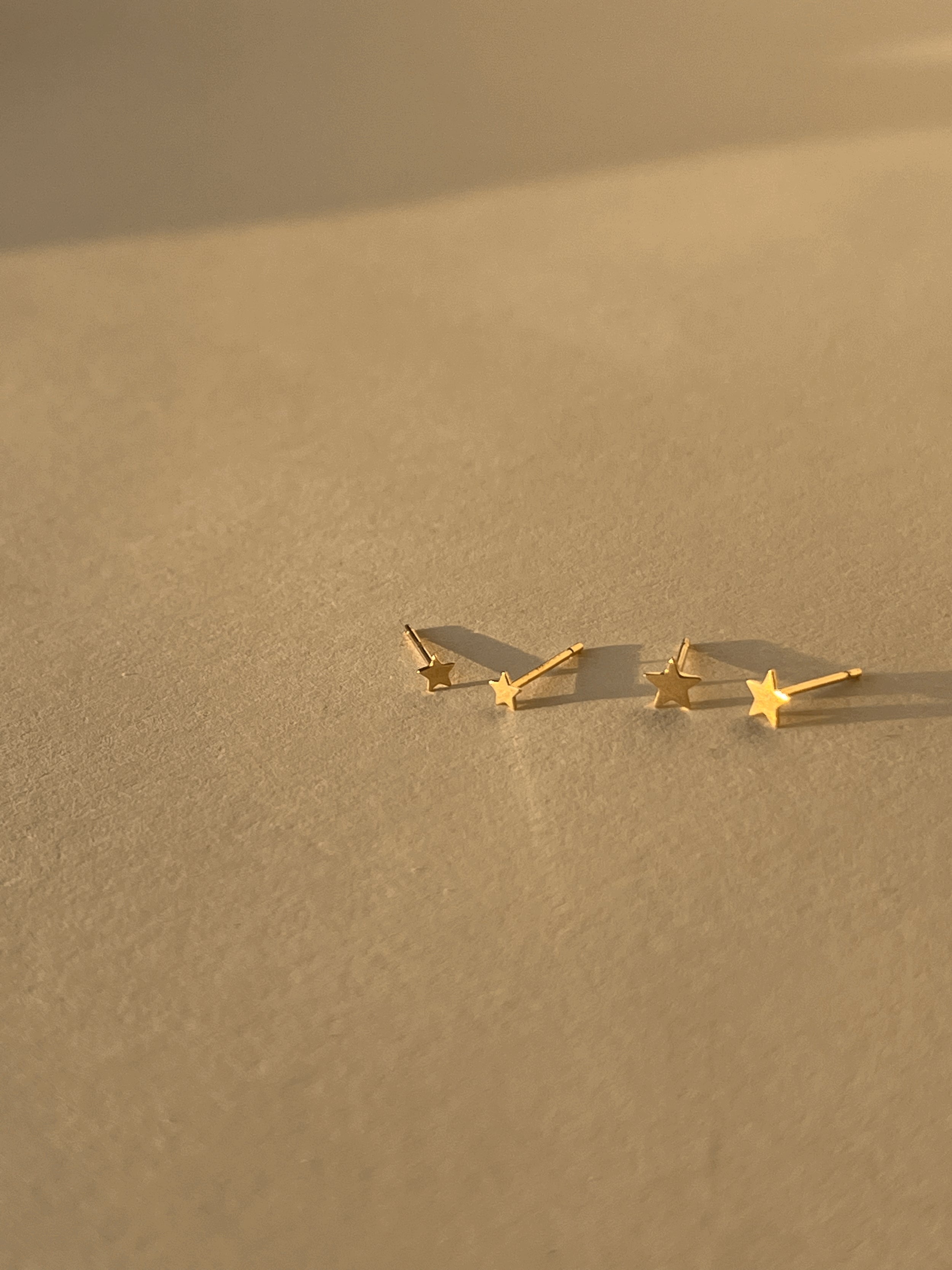 Close-up of the 3mm and 4mm Tiny Star Stud Earrings in 14k solid yellow gold displayed side by side on a neutral backdrop