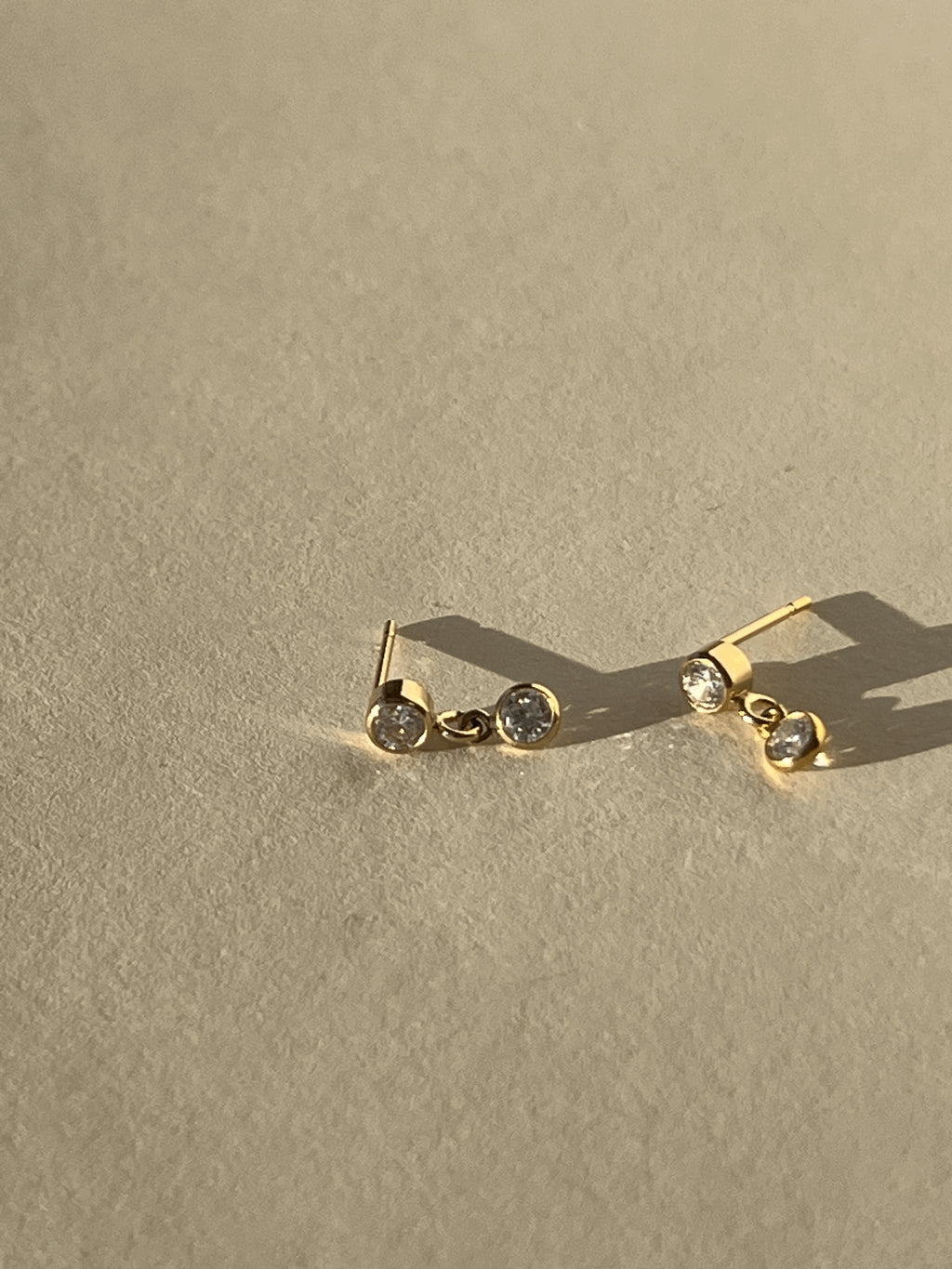Close-up product shot of Thalken’s 3mm gold-filled cubic zirconia stud and drop earrings on a neutral background, highlighting the bezel setting and drop