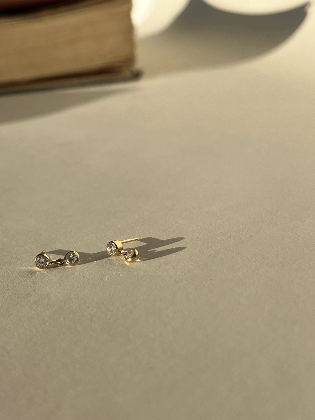  Artful product photo of Thalken’s gold-filled cubic zirconia stud and drop earrings with a book in the background, creating a warm lifestyle aesthetic