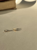  Artful product photo of Thalken’s gold-filled cubic zirconia stud and drop earrings with a book in the background, creating a warm lifestyle aesthetic