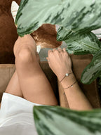 Model in a white skirt sitting beside a plant, bird’s-eye view of the Thalken® sparkle mantra bracelet stacked with the Moon Charged bracelet