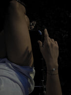 Alternate angle nighttime bird’s-eye view of model in white pajama shorts wearing the Thalken® sparkle mantra bracelet stacked with the Moon Charged bracelet arm on armrest