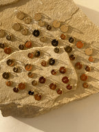 All twenty-six uppercase letters stamped on yellow gold-filled 7mm and 9mm disc charms, displayed without chains on a natural rock to show sizing and style