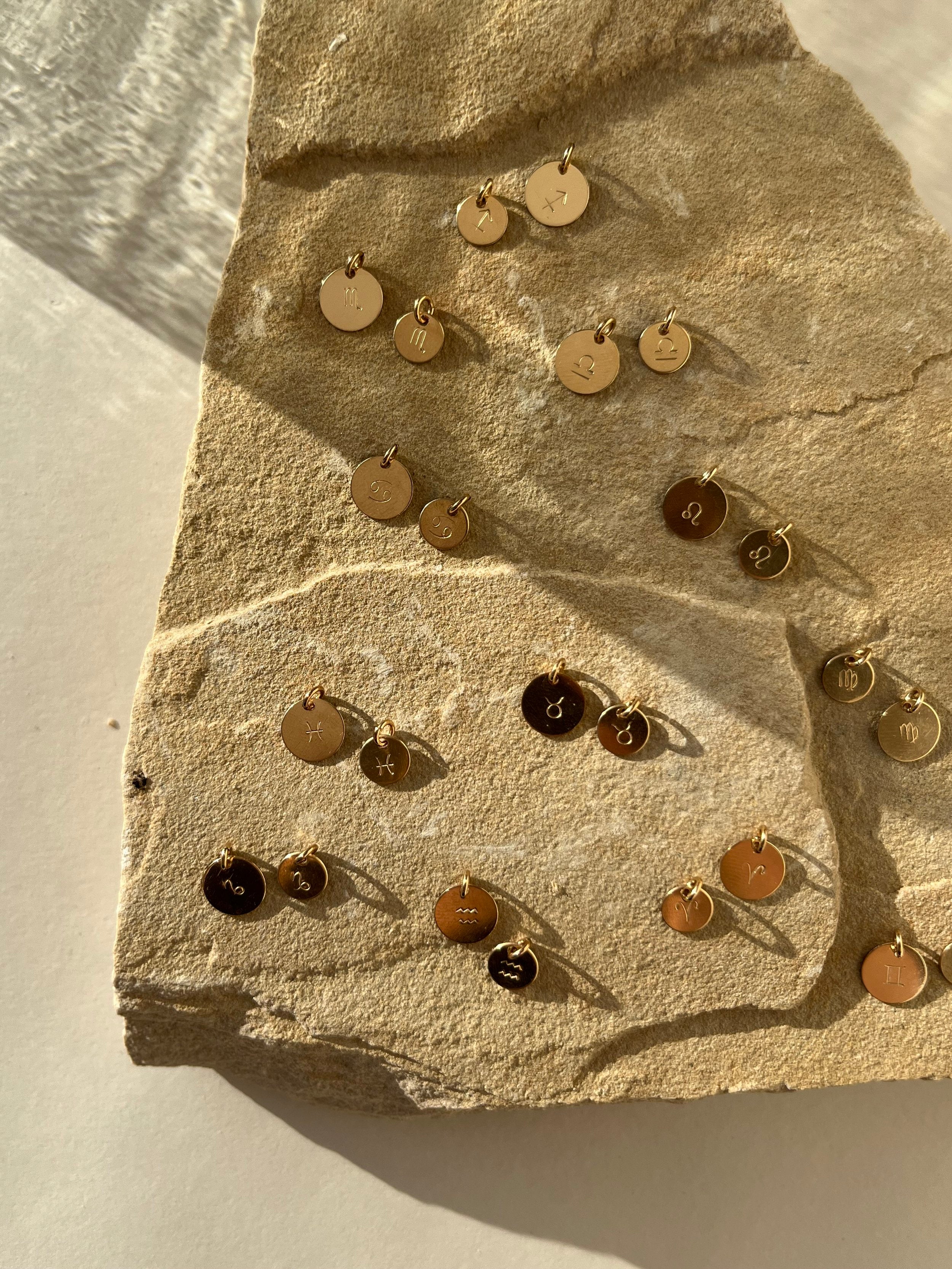 Yellow gold-filled 7mm and 9mm zodiac disc charms displayed on a natural rock, shown without chains