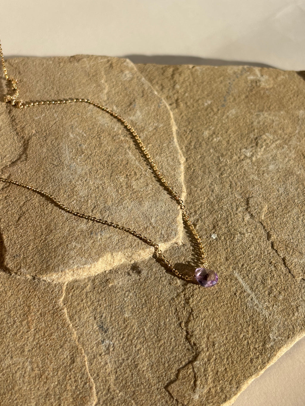 Natural purple amethyst stone necklace draped over natural rock in warm light