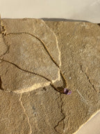 Natural purple amethyst stone necklace draped over natural rock in warm light