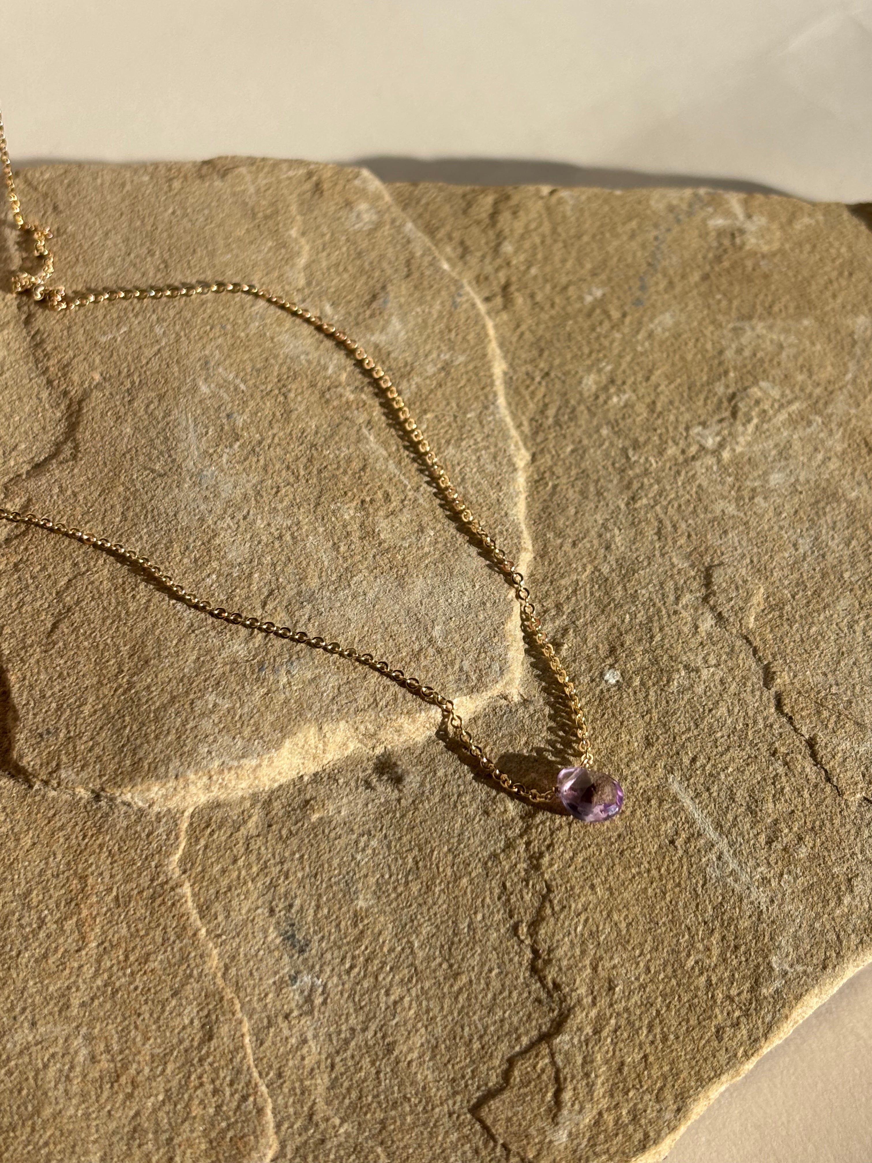 Natural purple amethyst stone necklace draped over natural rock in warm light