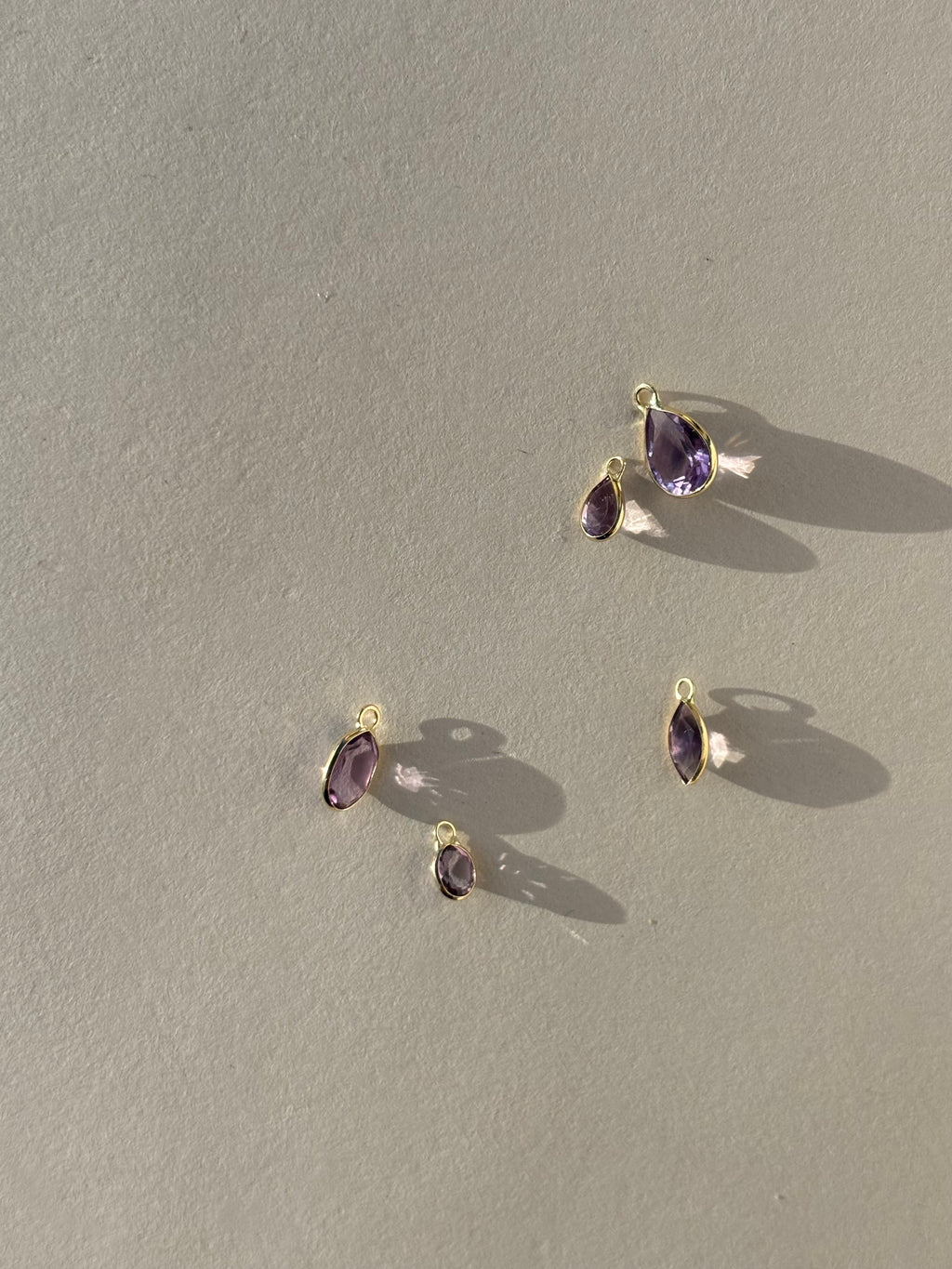 Collection of Thalken 14k solid gold single drop earring charms with natural amethyst in pear, marquise, and oval shapes, displayed unattached to hoops for mix-and-match styling