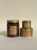 Photo of Thalken’s "...and we started a podcast"  candle shown in three vessel options — sleek gold tins (2oz and 6oz) and a soft-glow glass jar (8oz). Earthy scent profile with notes of sandalwood, cardamom, and good conversation.