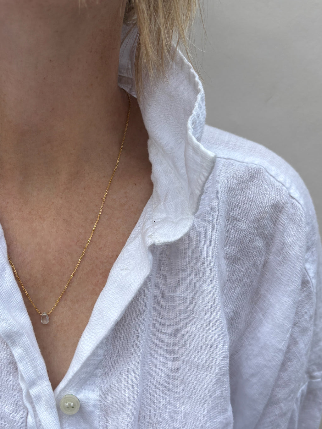 Dainty Thalken aquamarine drop necklace on woman wearing white linen button down shirt