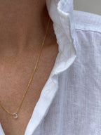 Close-up of dainty Thalken aquamarine drop necklace on woman wearing white linen button down shirt