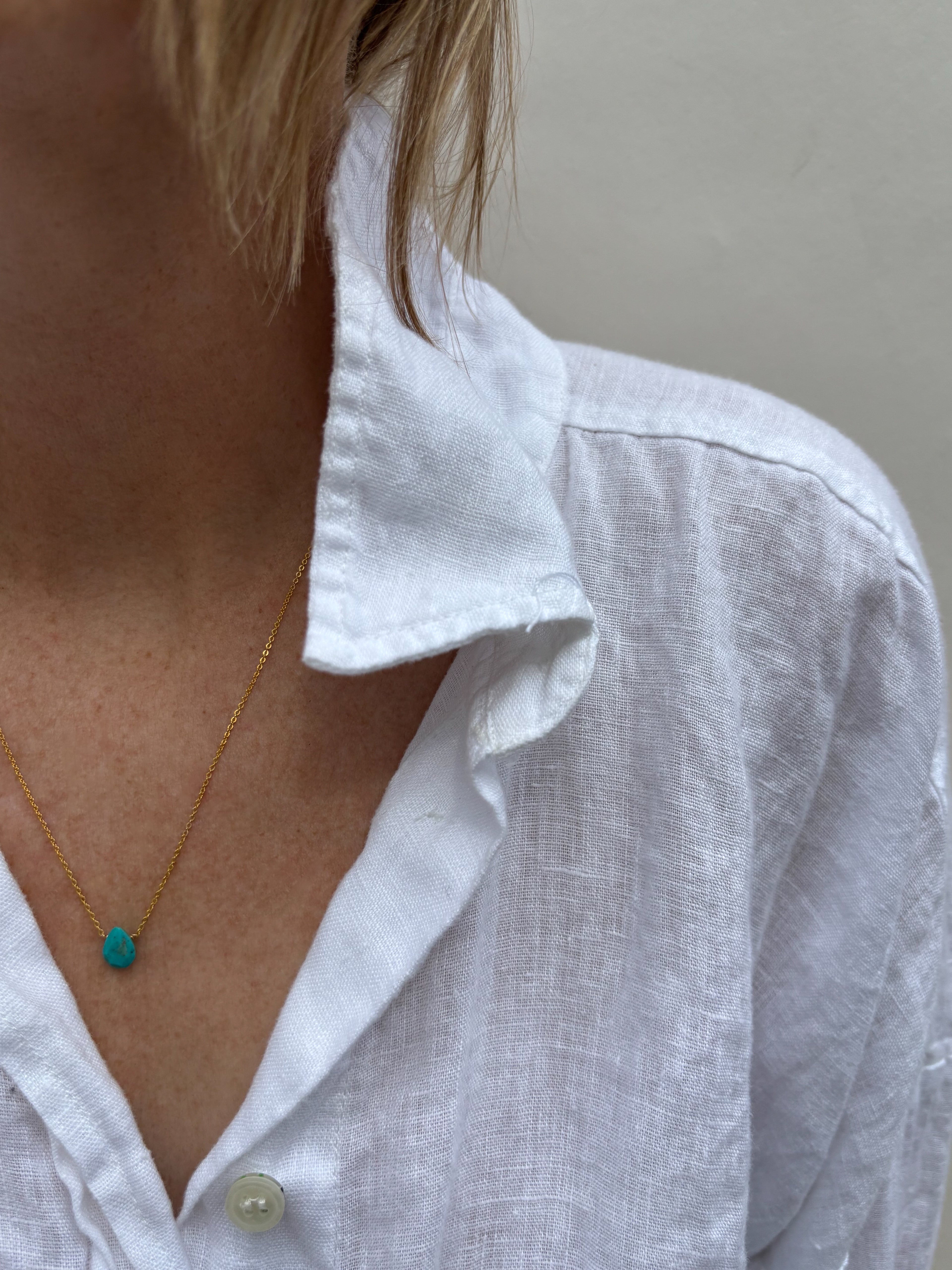 Model wearing a white linen button down shirt in a dainty Arizona turquoise drop necklace in yellow gold-filled 