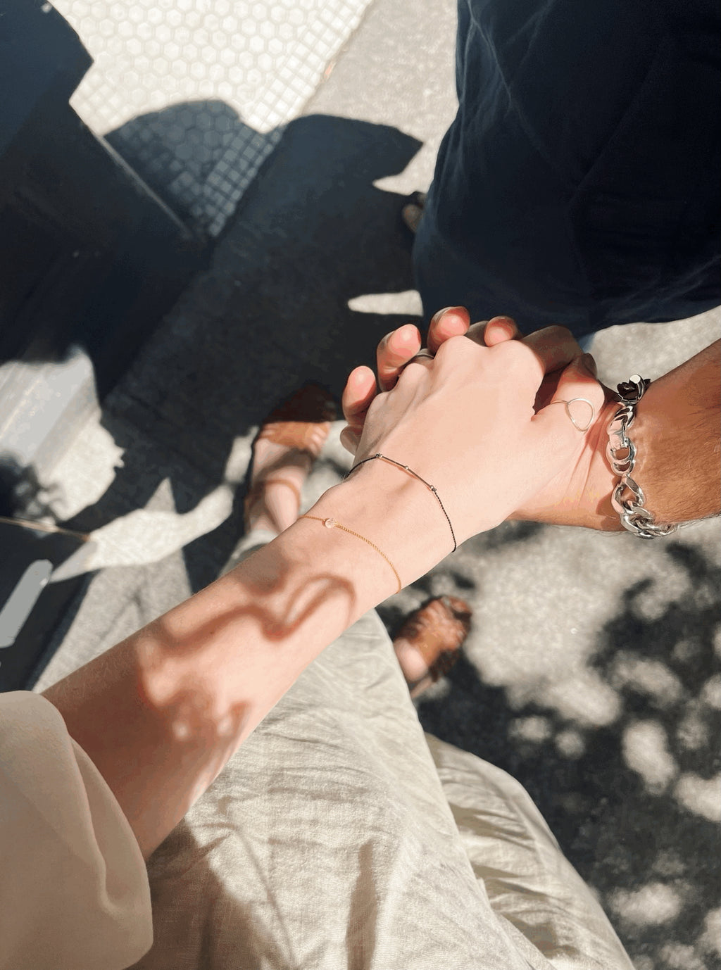 Outdoors, model’s hands intertwined with another’s in an artistic shot, showcasing the Thalken® Drop of Sunshine bracelet layered with the Thalken® Balance Bracelet