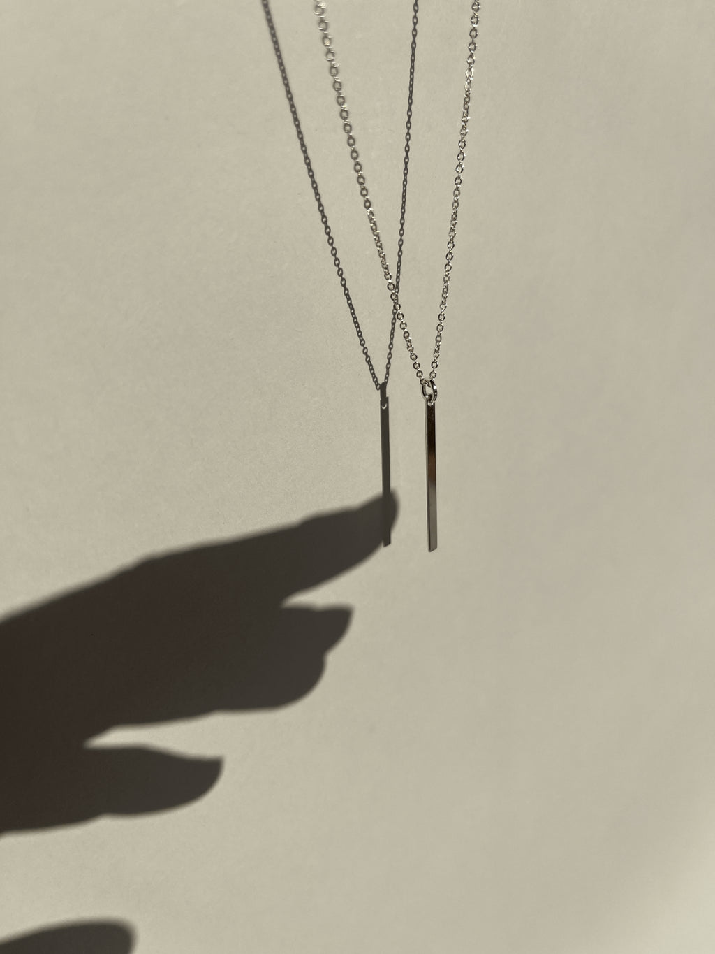 Different angle of sterling silver Bar Necklace suspended in air with shadow of a hand reaching toward it