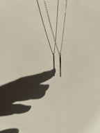 Different angle of sterling silver Bar Necklace suspended in air with shadow of a hand reaching toward it