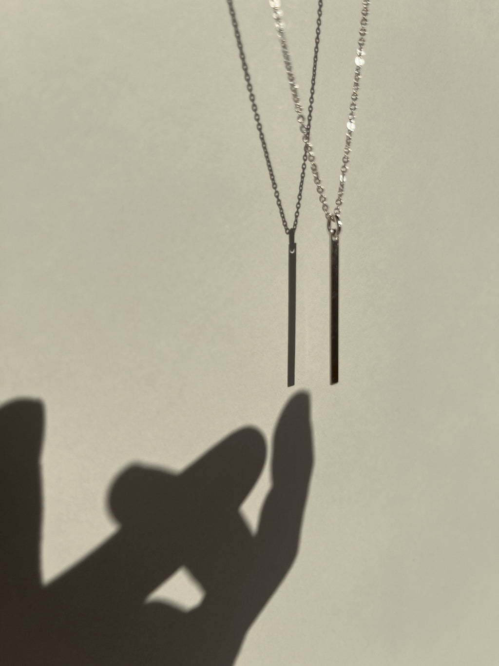 Sterling silver Bar Necklace suspended in air with shadow of a hand reaching toward it