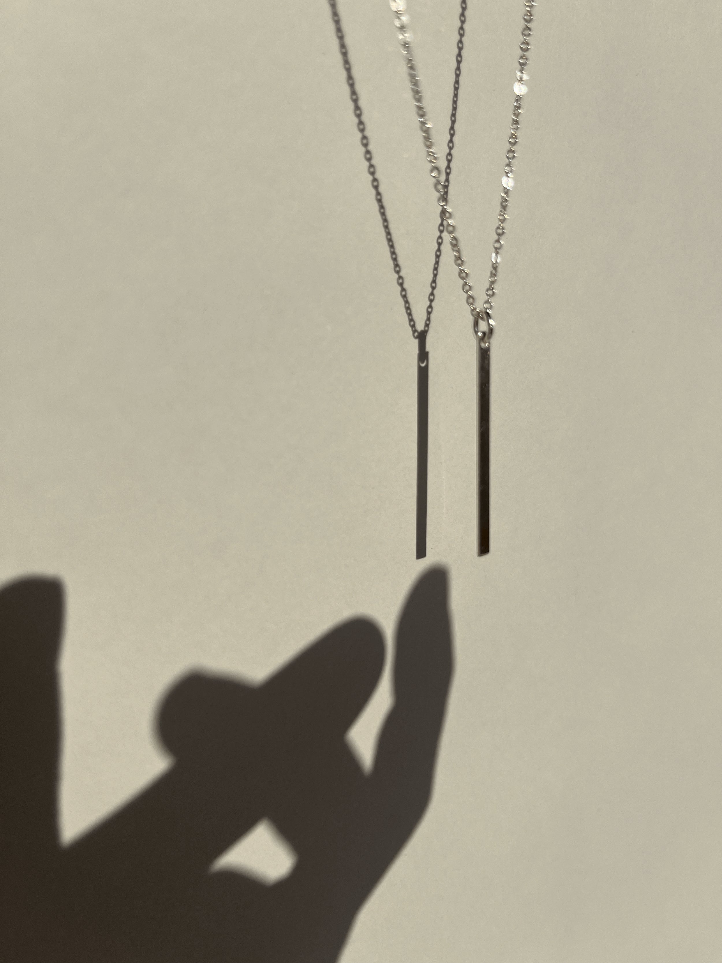 Sterling silver Bar Necklace suspended in air with shadow of a hand reaching toward it