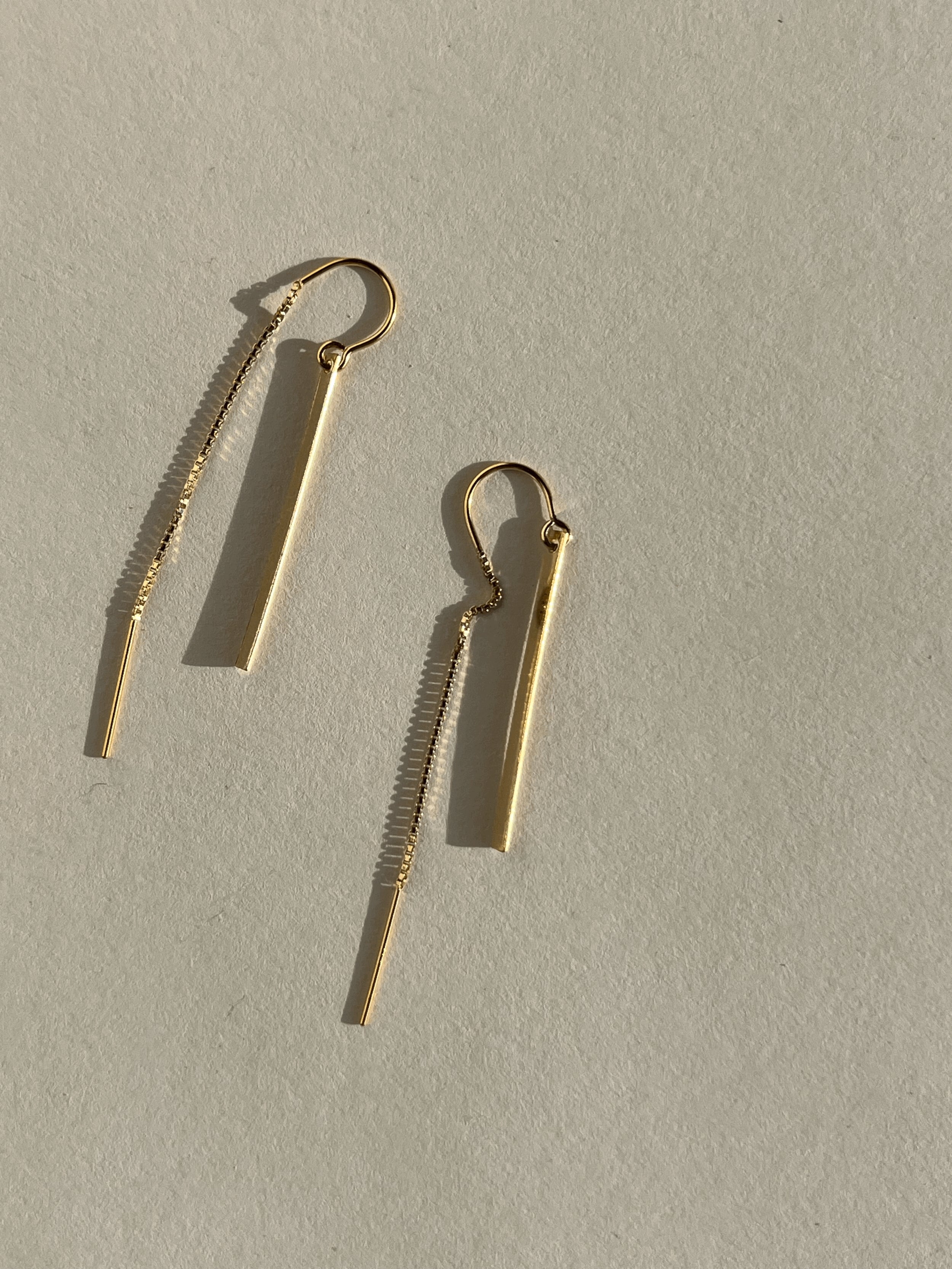 Yellow gold-filled Bar Threader Earrings displayed on a cream background, shown from the front angle highlighting their sleek minimalist design