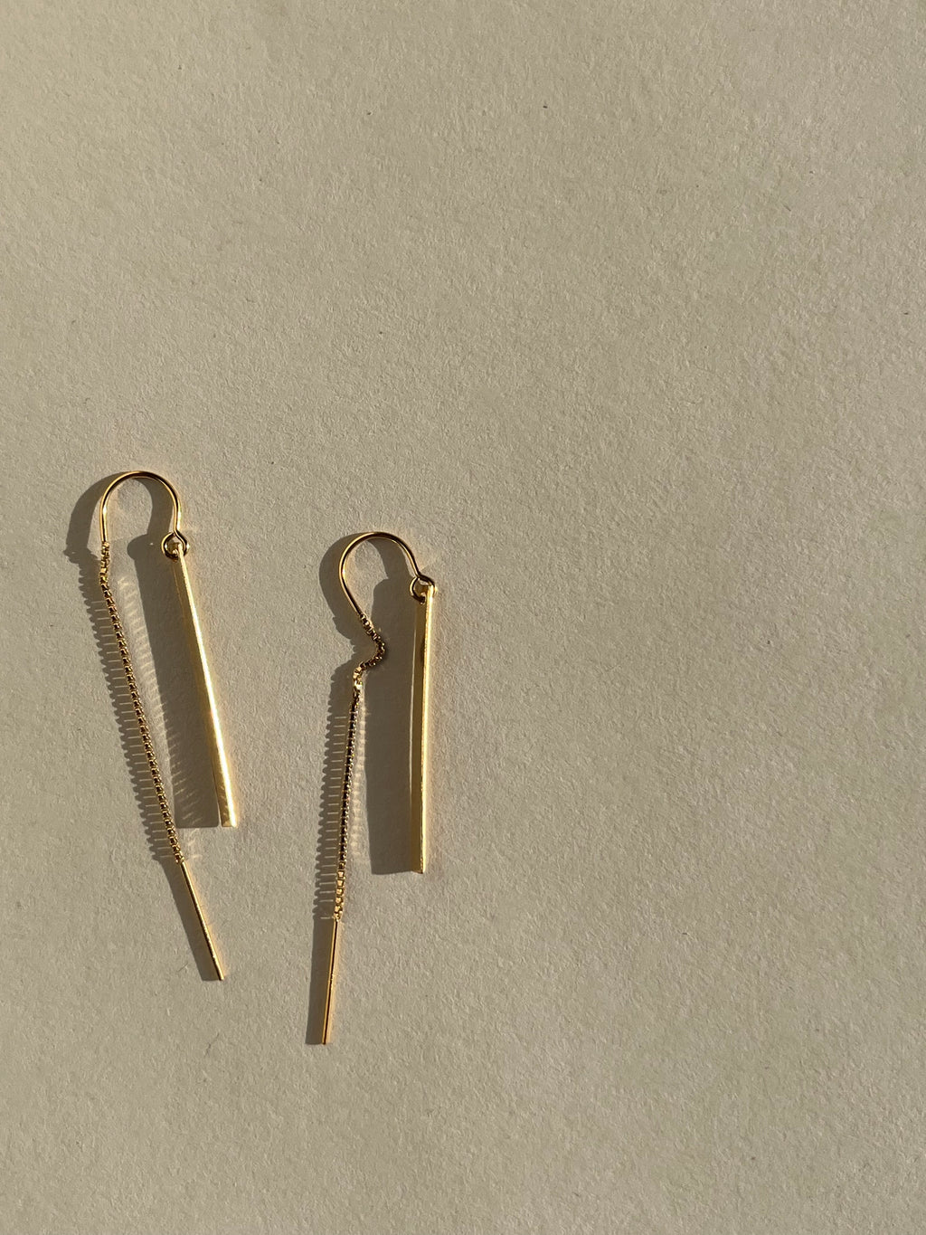 Yellow gold-filled Bar Threader Earrings photographed from a side angle on a cream background, showcasing their delicate threader style and smooth finish
