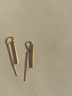 Yellow gold-filled Bar Threader Earrings photographed from a side angle on a cream background, showcasing their delicate threader style and smooth finish