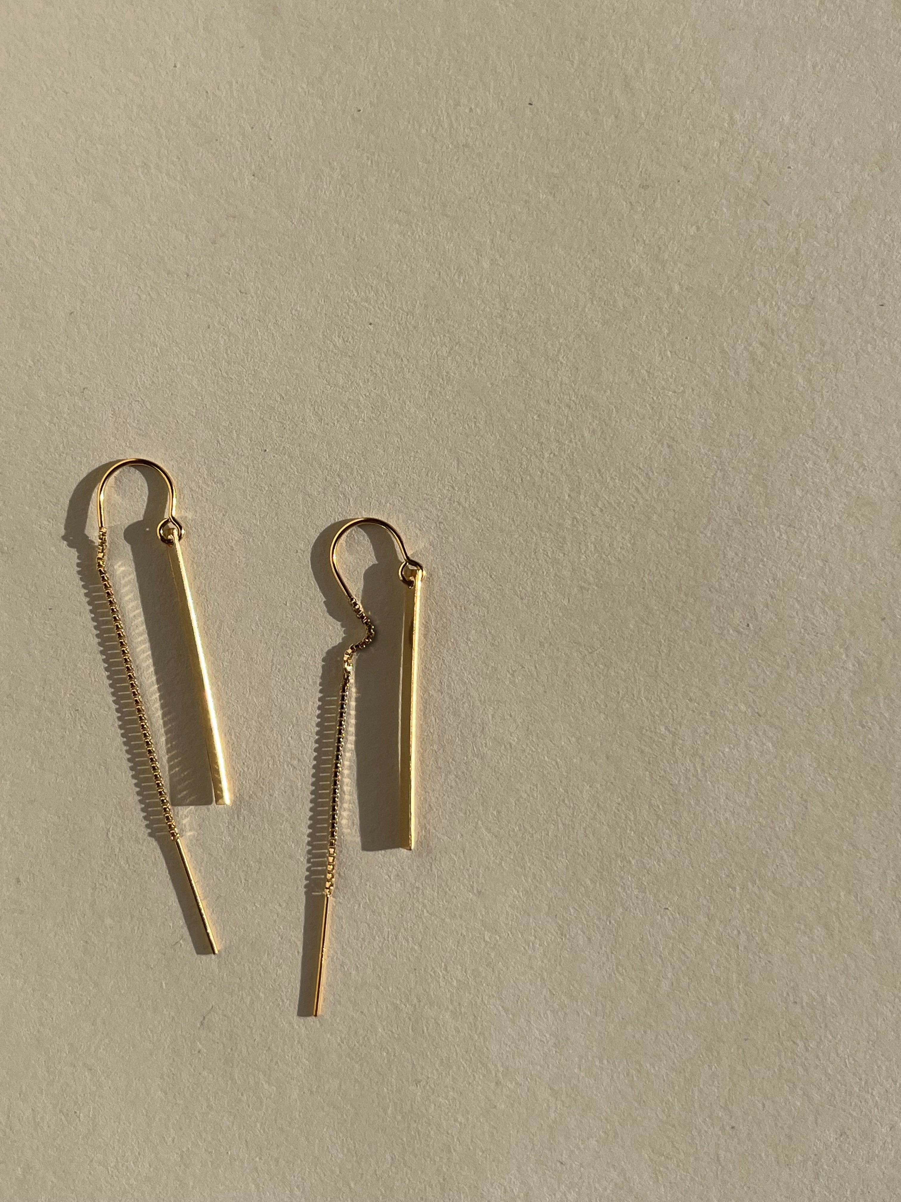 Yellow gold-filled Bar Threader Earrings photographed from a side angle on a cream background, showcasing their delicate threader style and smooth finish