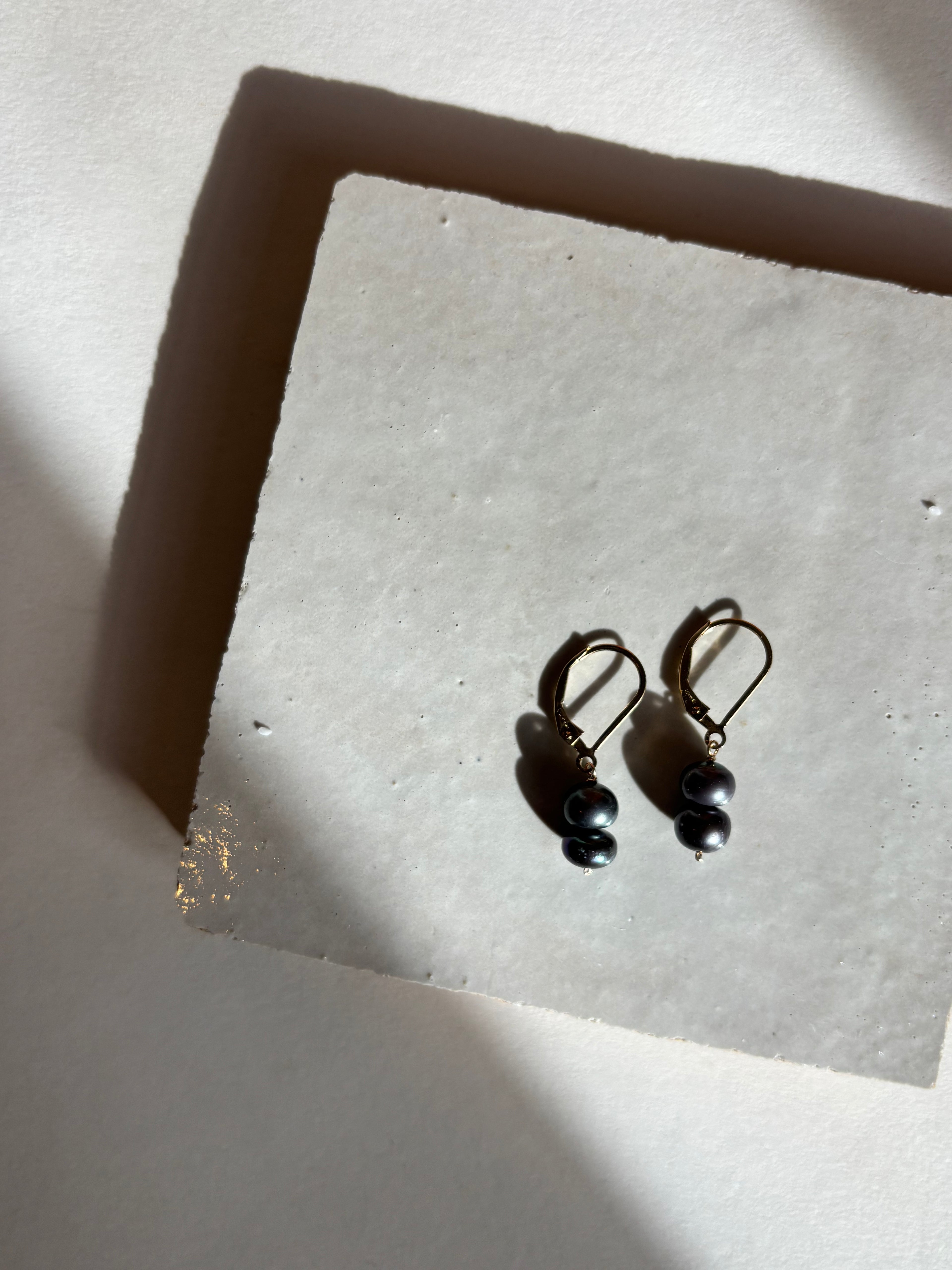 Close-up of the midnight(black) double pearl drop detail on leverback earrings with warm, moody lighting.