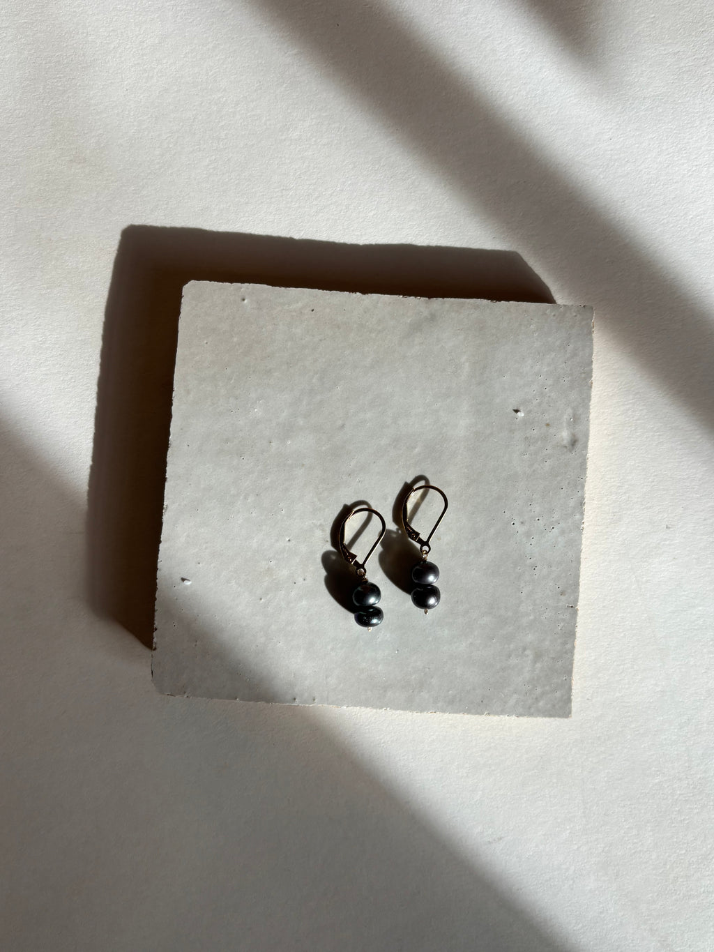 Black(midnight) double pearl drop on leverback earrings with warm, moody lighting.