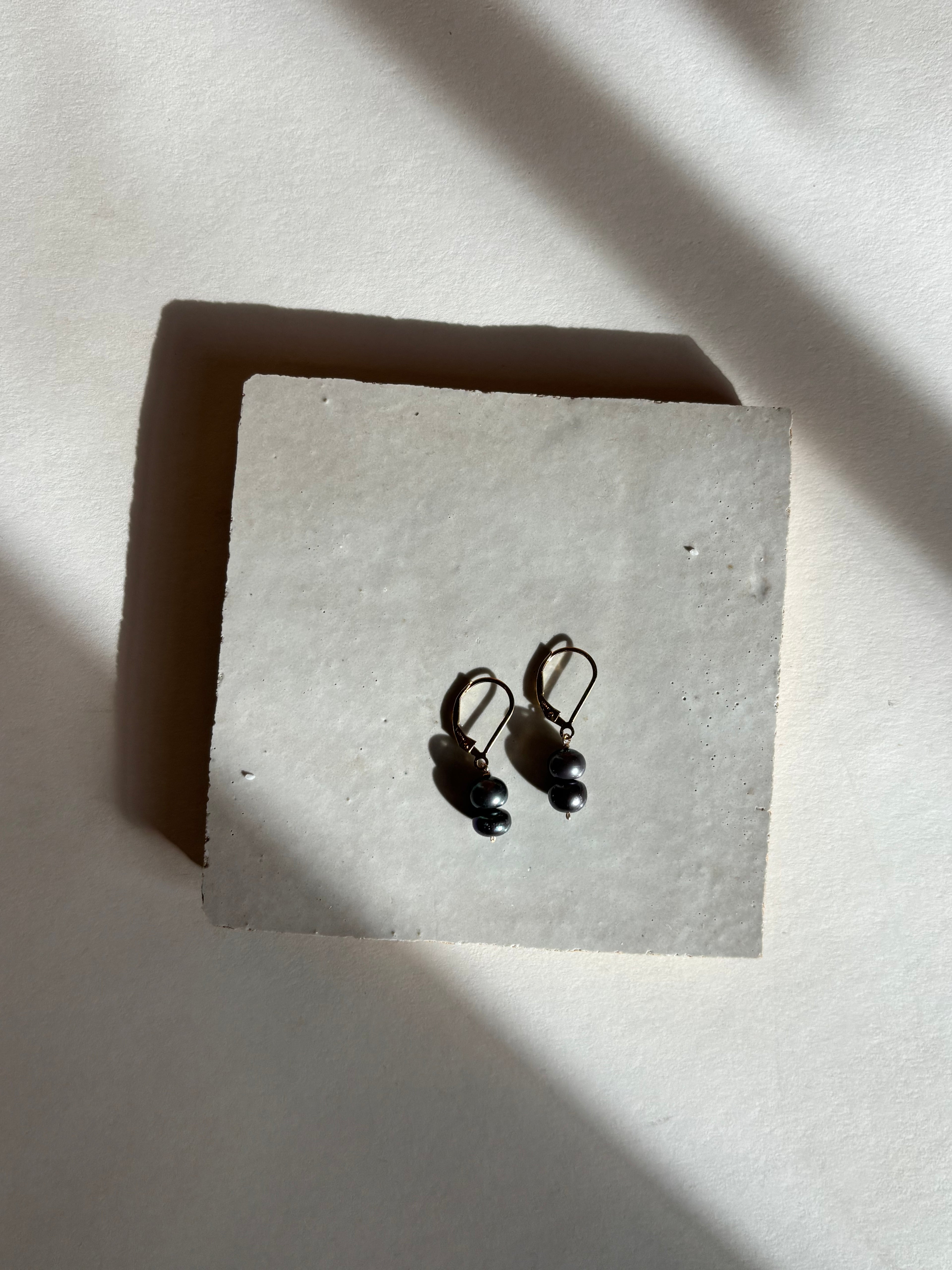 Black(midnight) double pearl drop on leverback earrings with warm, moody lighting.